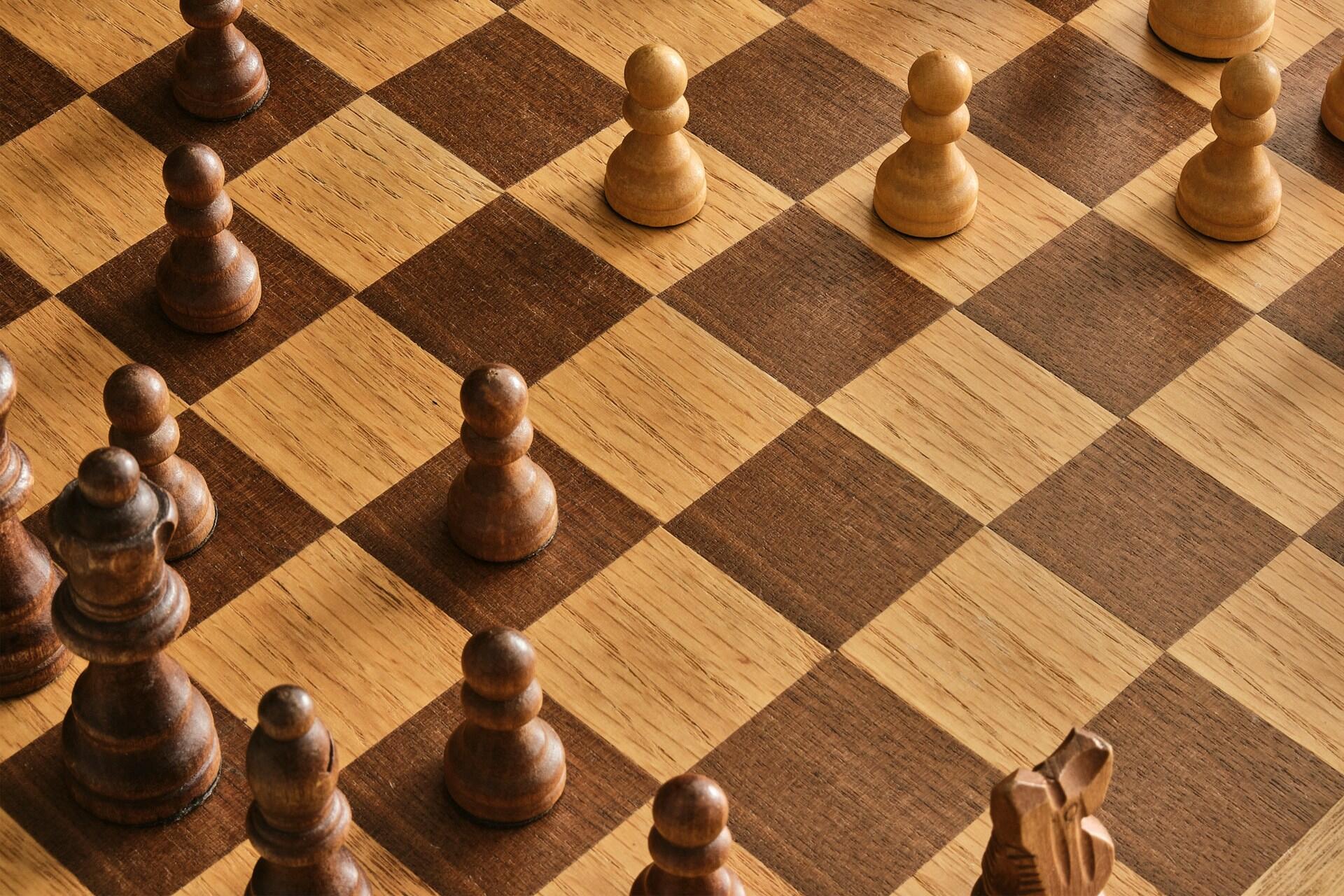 Wooden chessboard showing several pawns and pieces positioned across alternating light and dark squares.