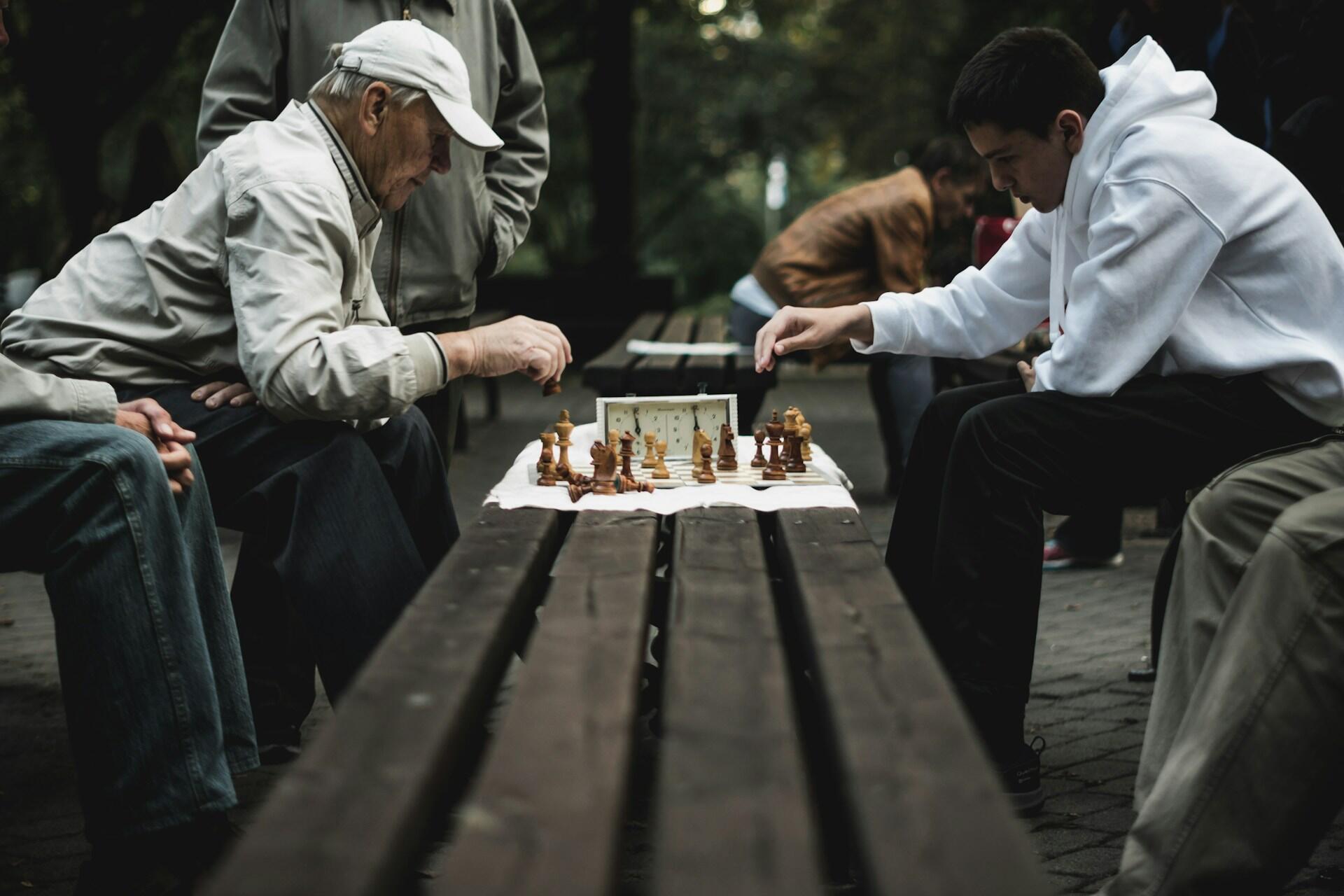 Two older men concentrating during an outdoor chess game at a park table.