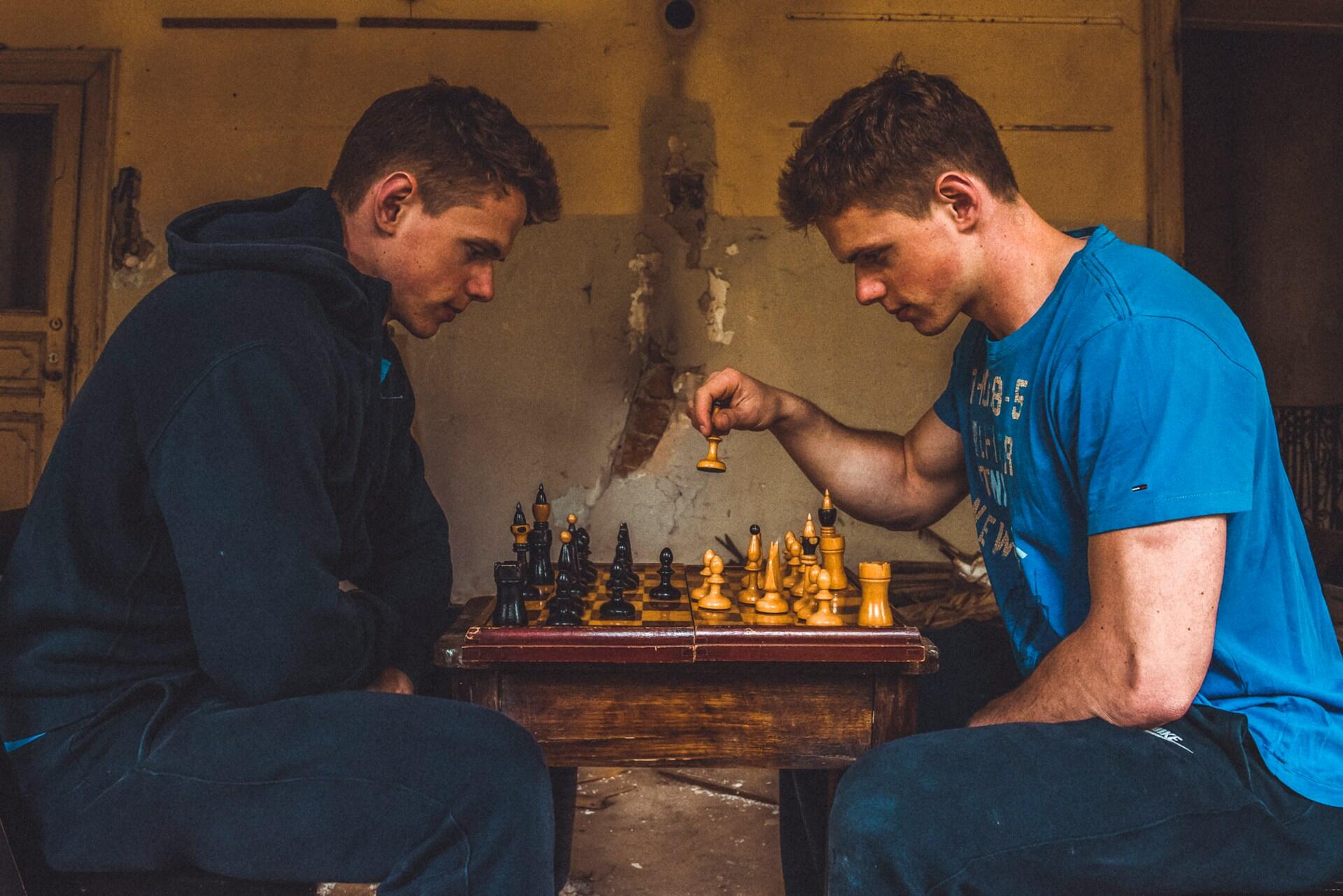 Two players sitting across from each other concentrating on a chess game at a small wooden table.