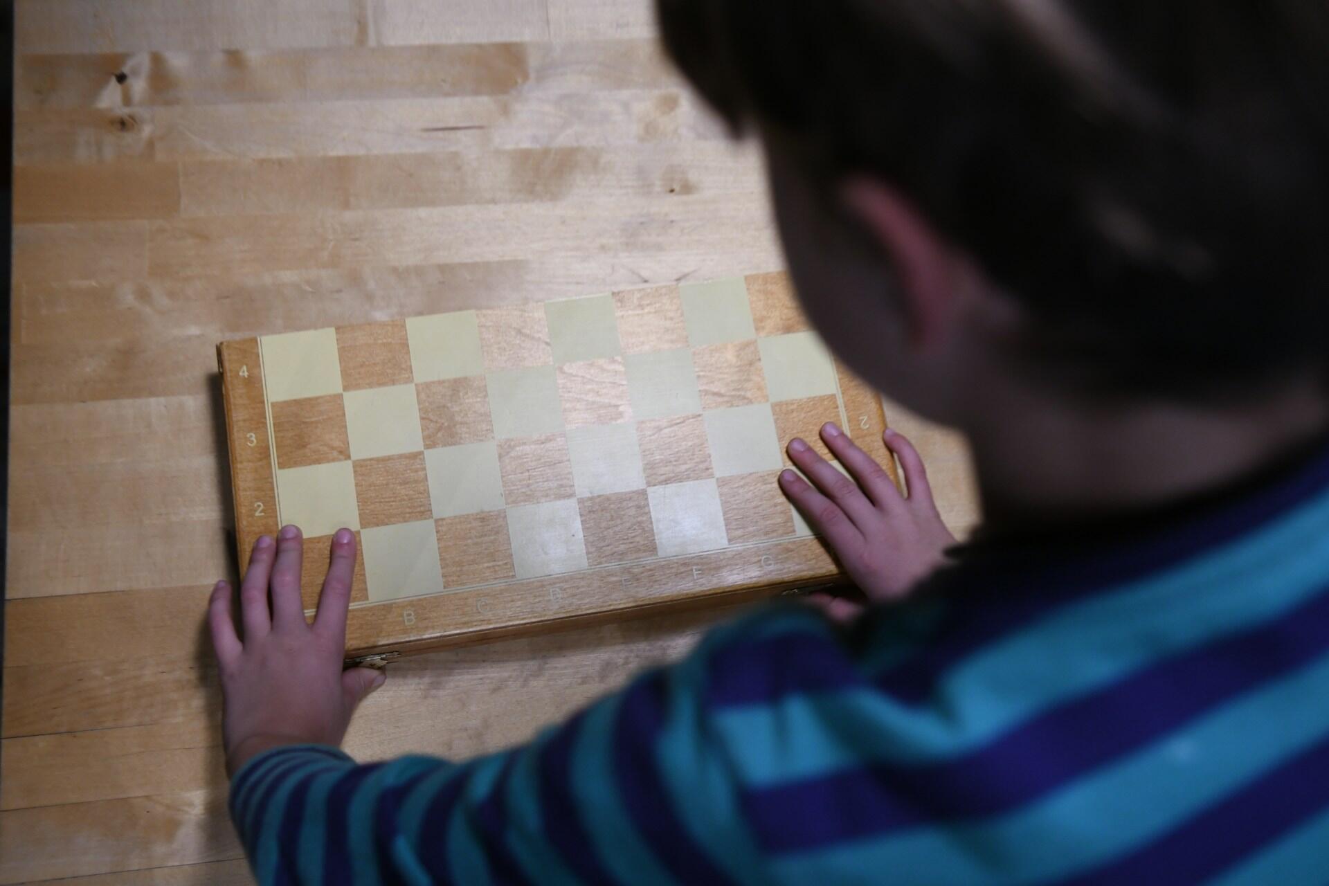 A child placing hands on a wooden chessboard while learning how to set up the board.
