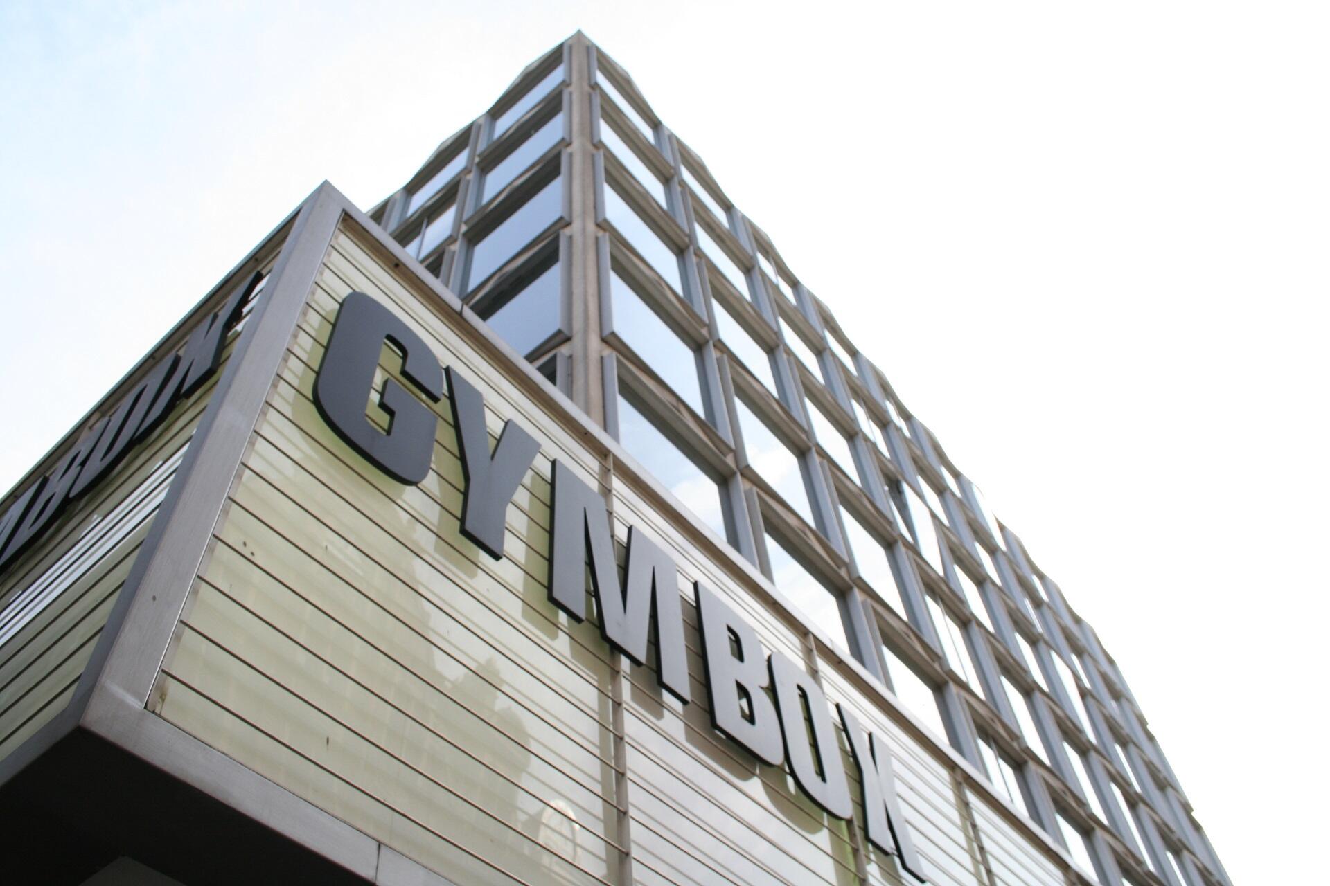 A large black sign on a tan-coloured building on a cloudy day.