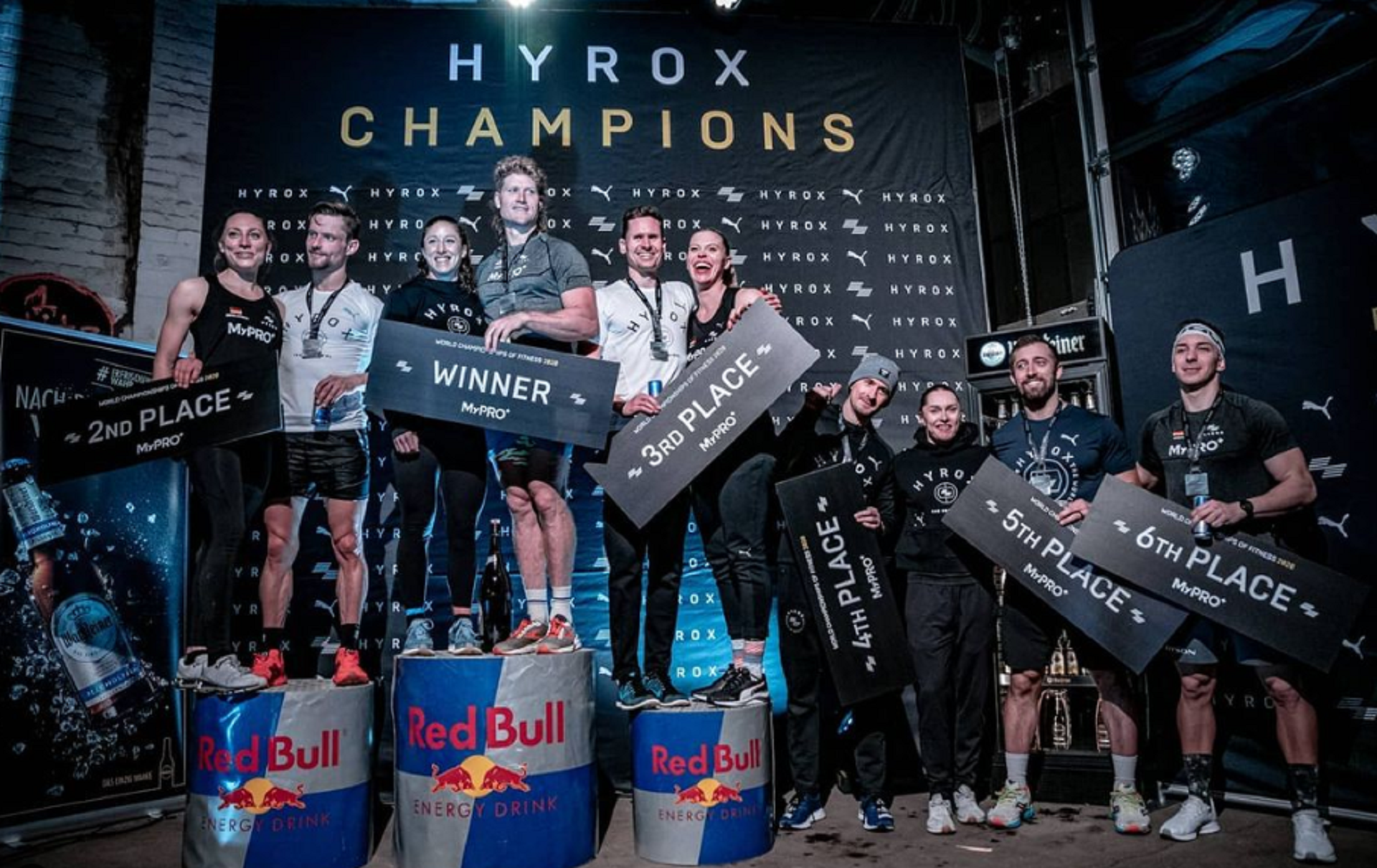 A group of athletes on podiums holding black and white signs in a gym. 