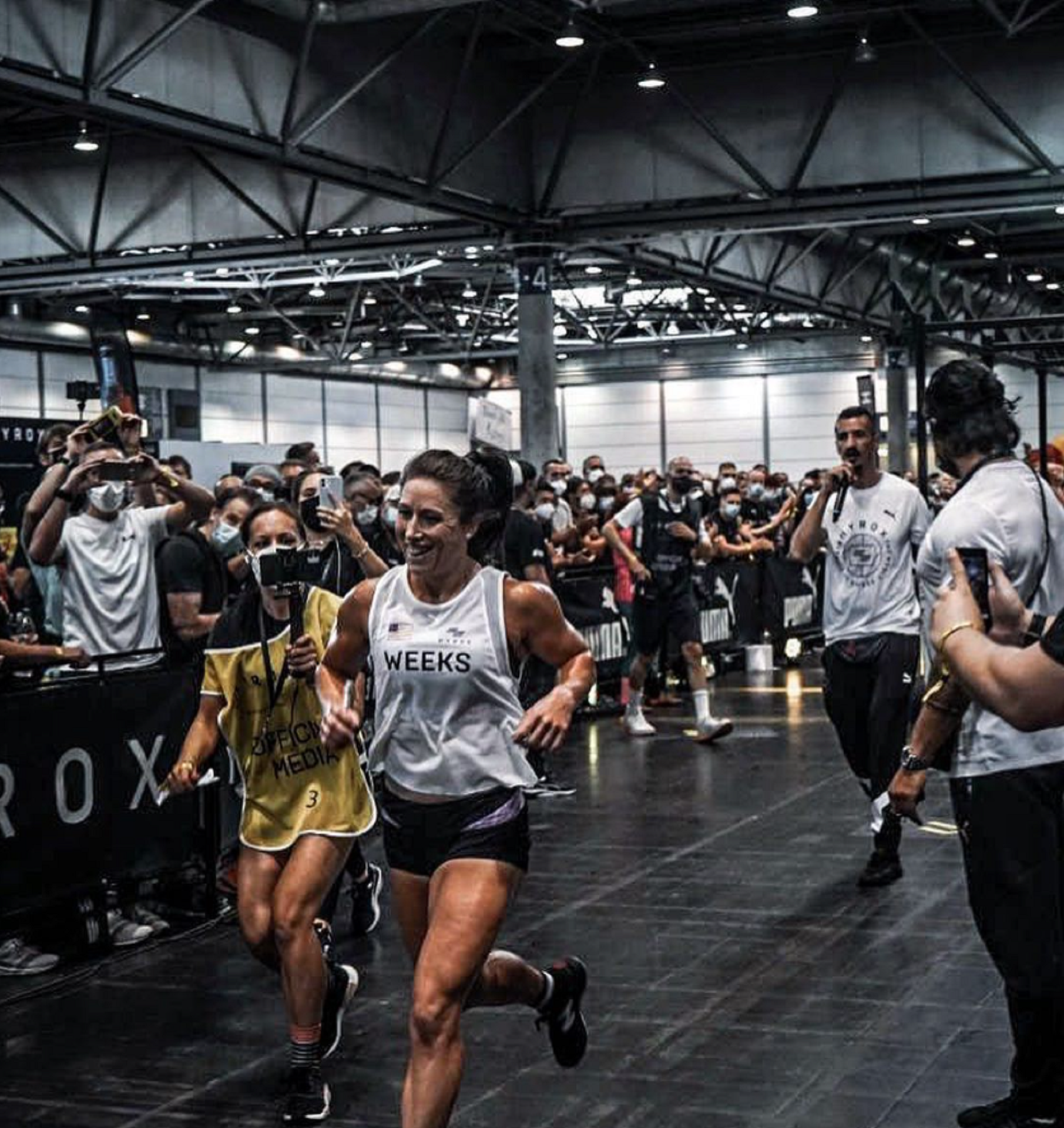 A person in a white shirt runs in an indoor space surrounded by spectators. 