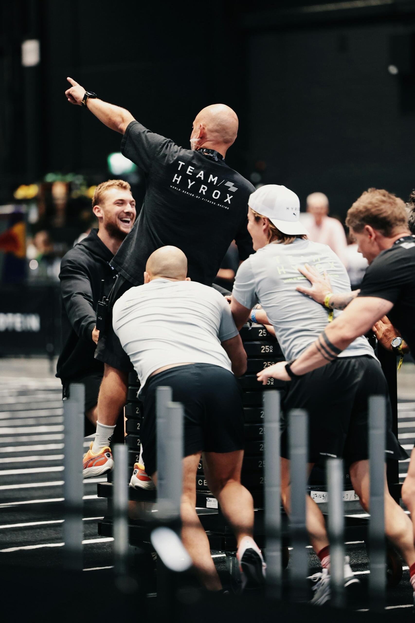 A man in a black shirt stands tall, surrounded by others in grey shirts who are smiling. 