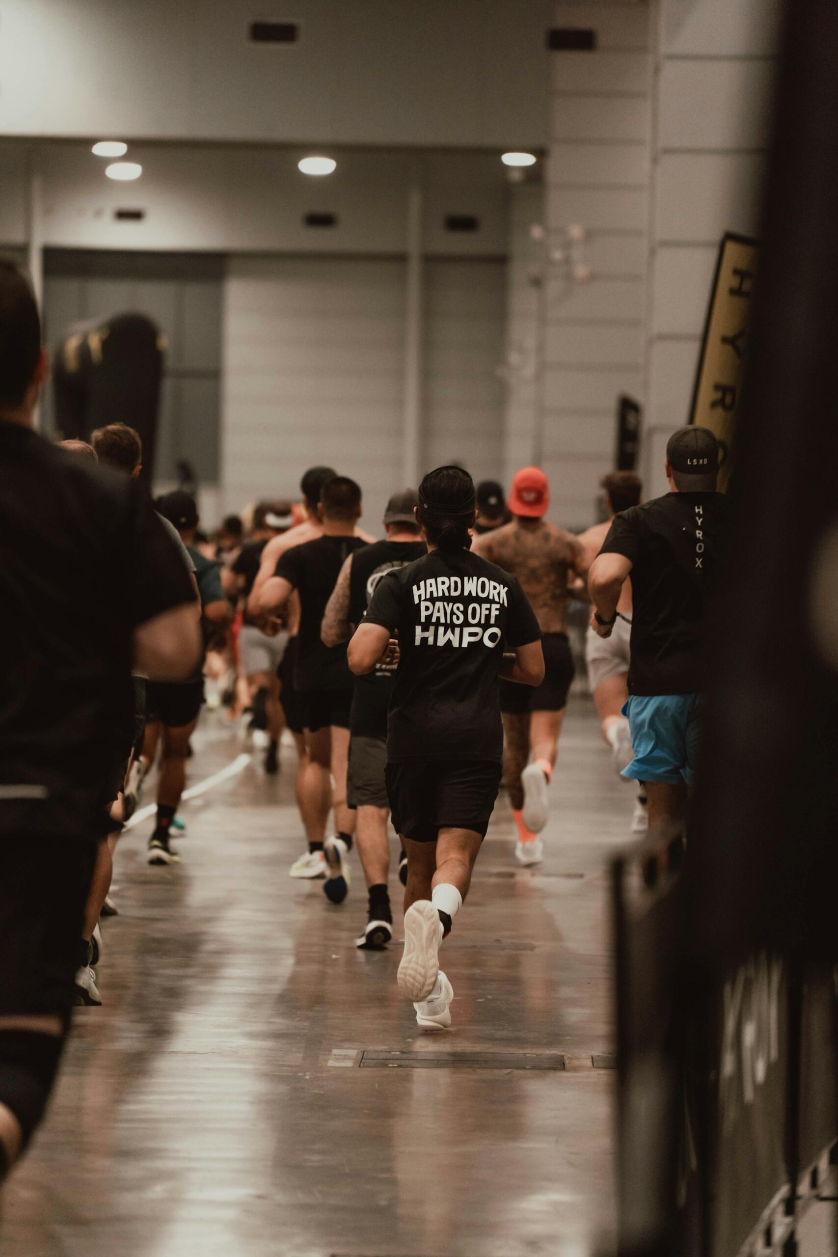 People wearing athletic clothing running indoors in a large hall. 
