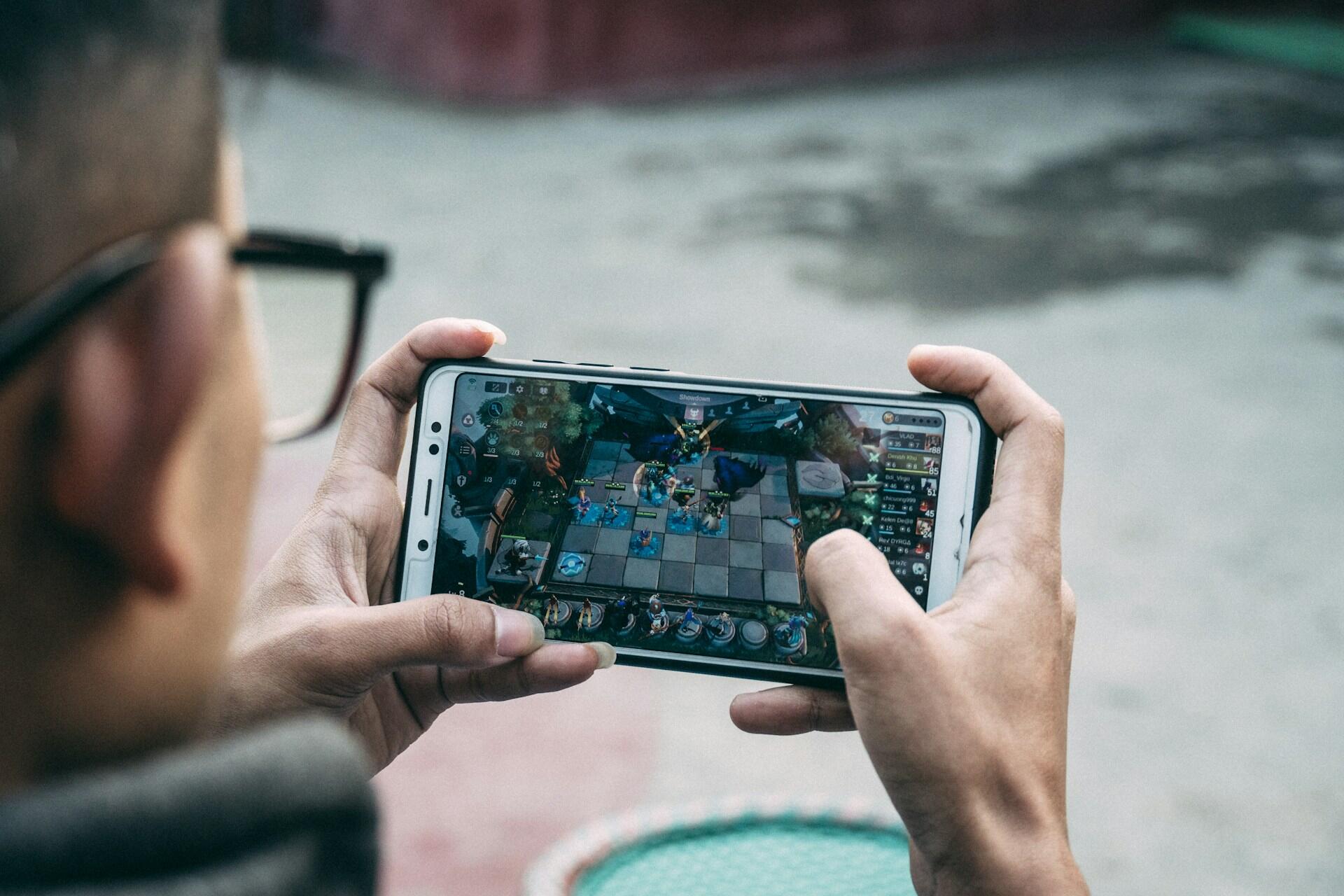 Person holding a smartphone while playing a strategy board game on screen