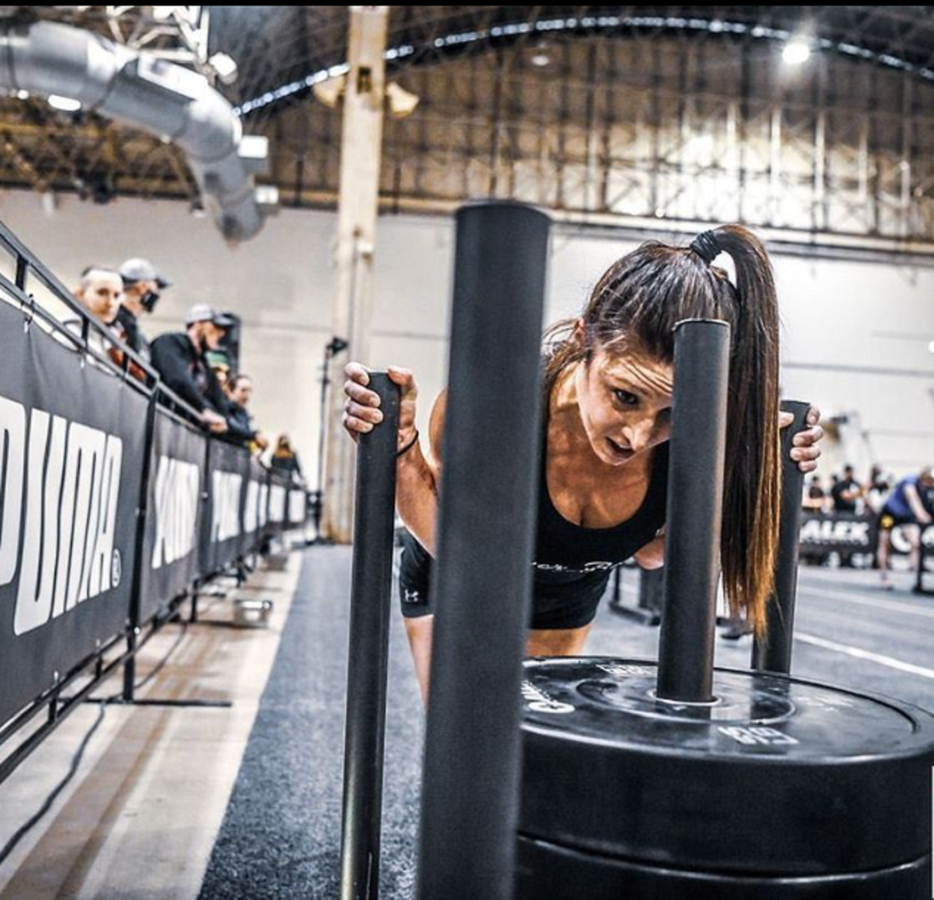 An athlete pushes a weighted sled in an indoors competition space. 