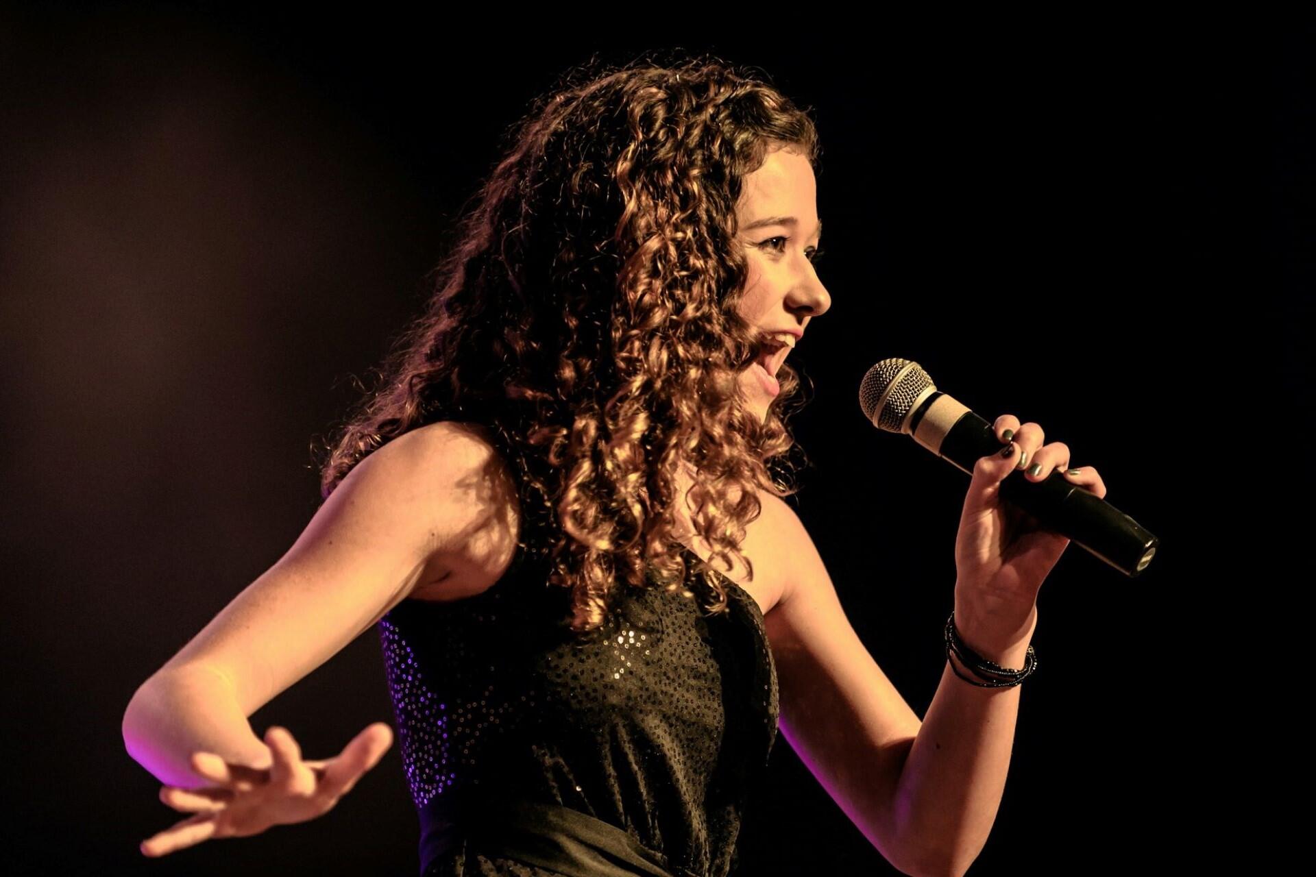 Young singer performing on stage with a microphone during a vocal performance
