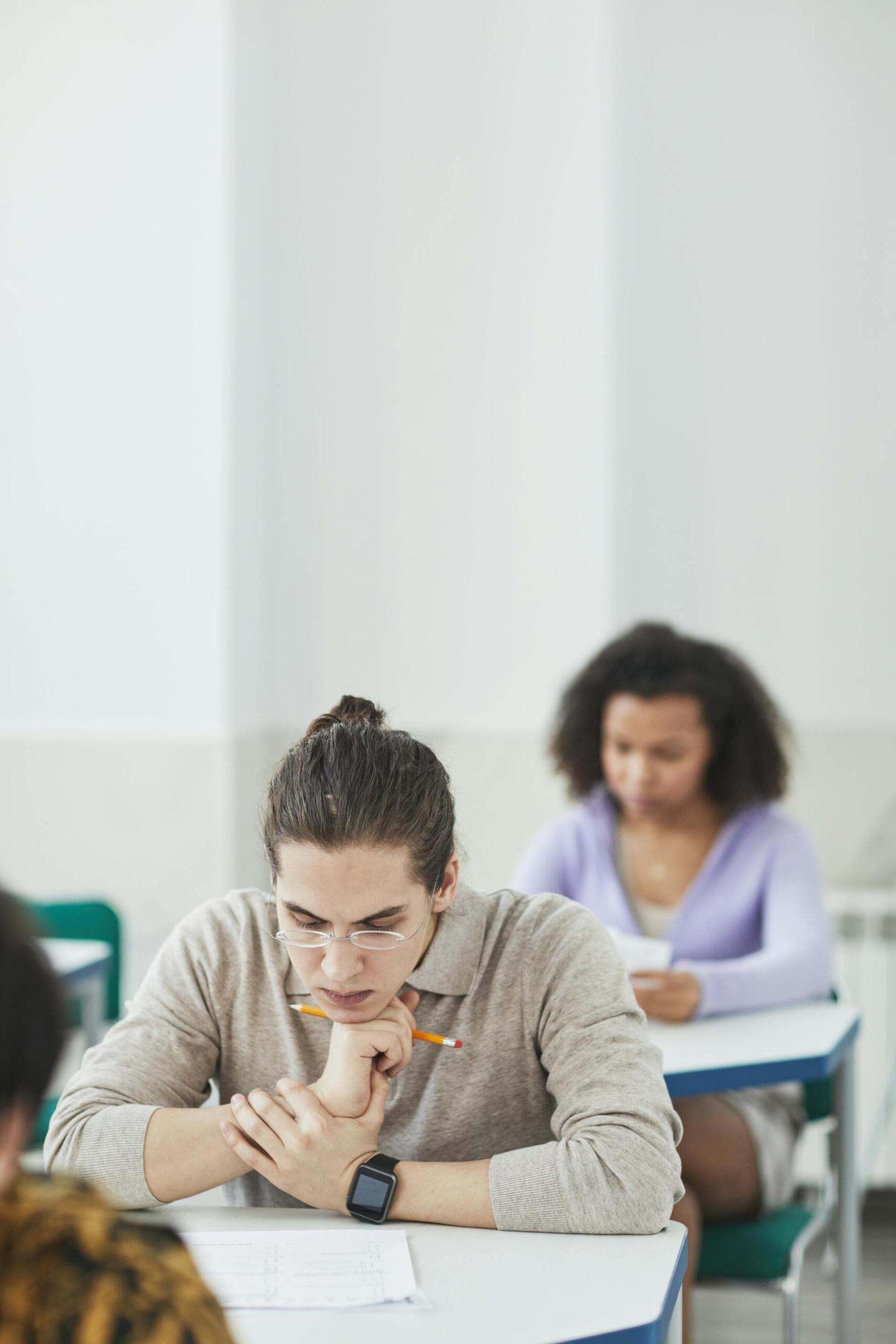 Students sitting at desks in a classroom, focused on writing or thinking during an exam or test session.
