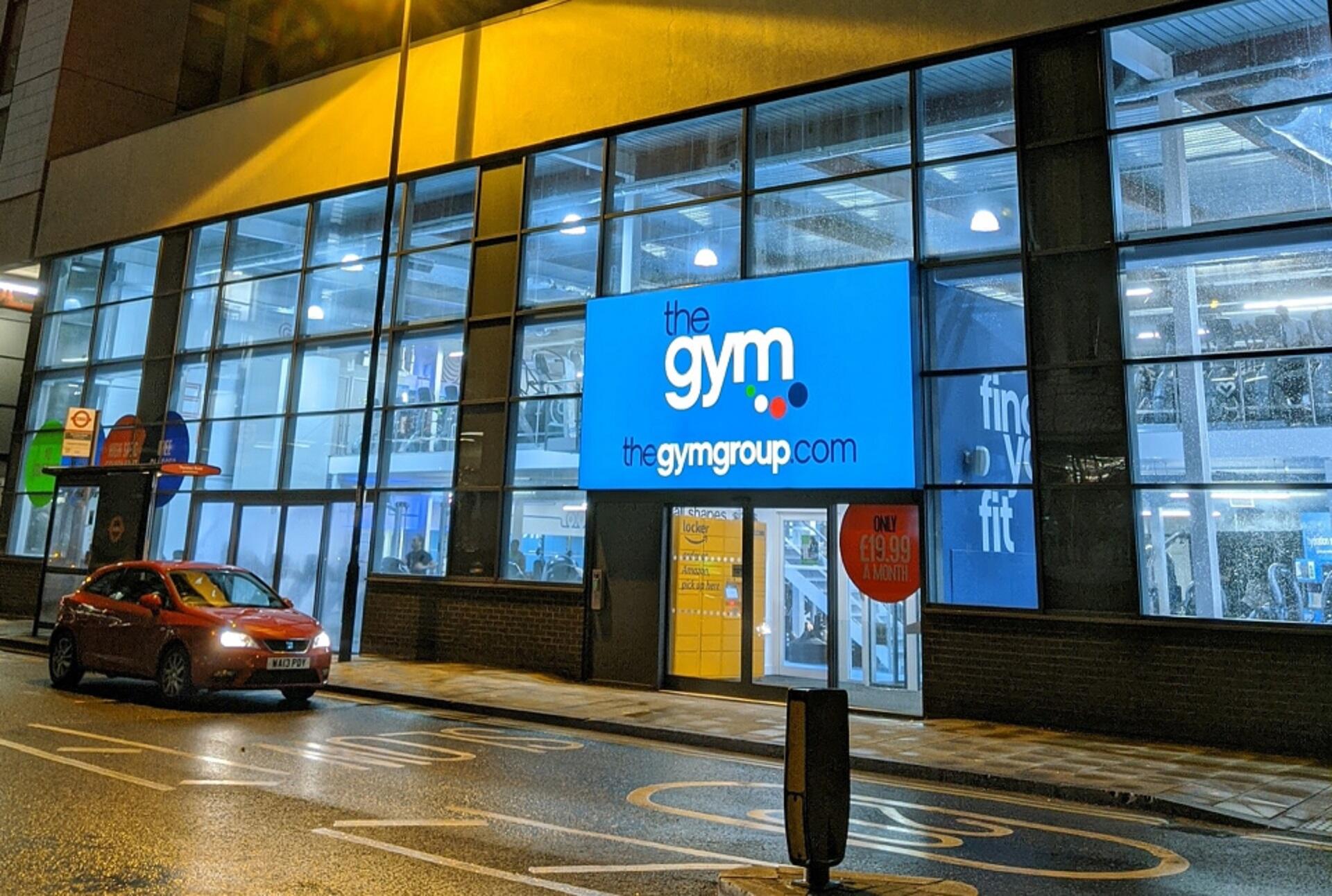 A bright blue sign on a glass-fronted building, lit up at night. 