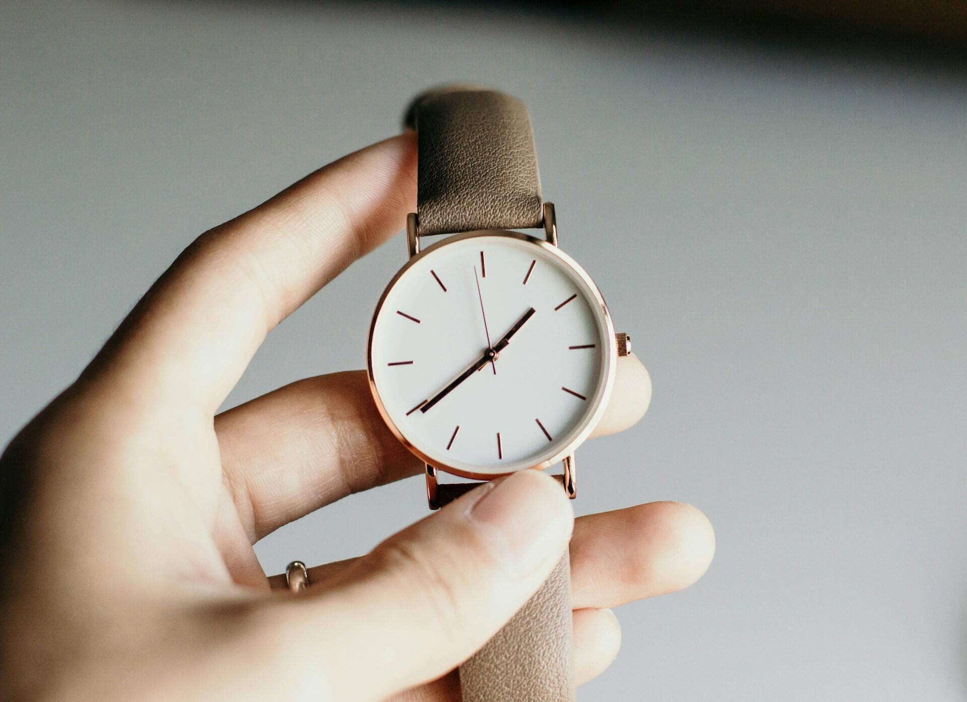 A person holding a watch with a brown band.