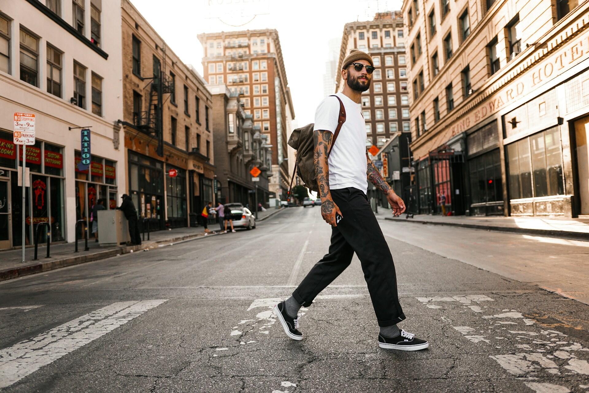 A man wearing a white tee shirt walking across a deserted street