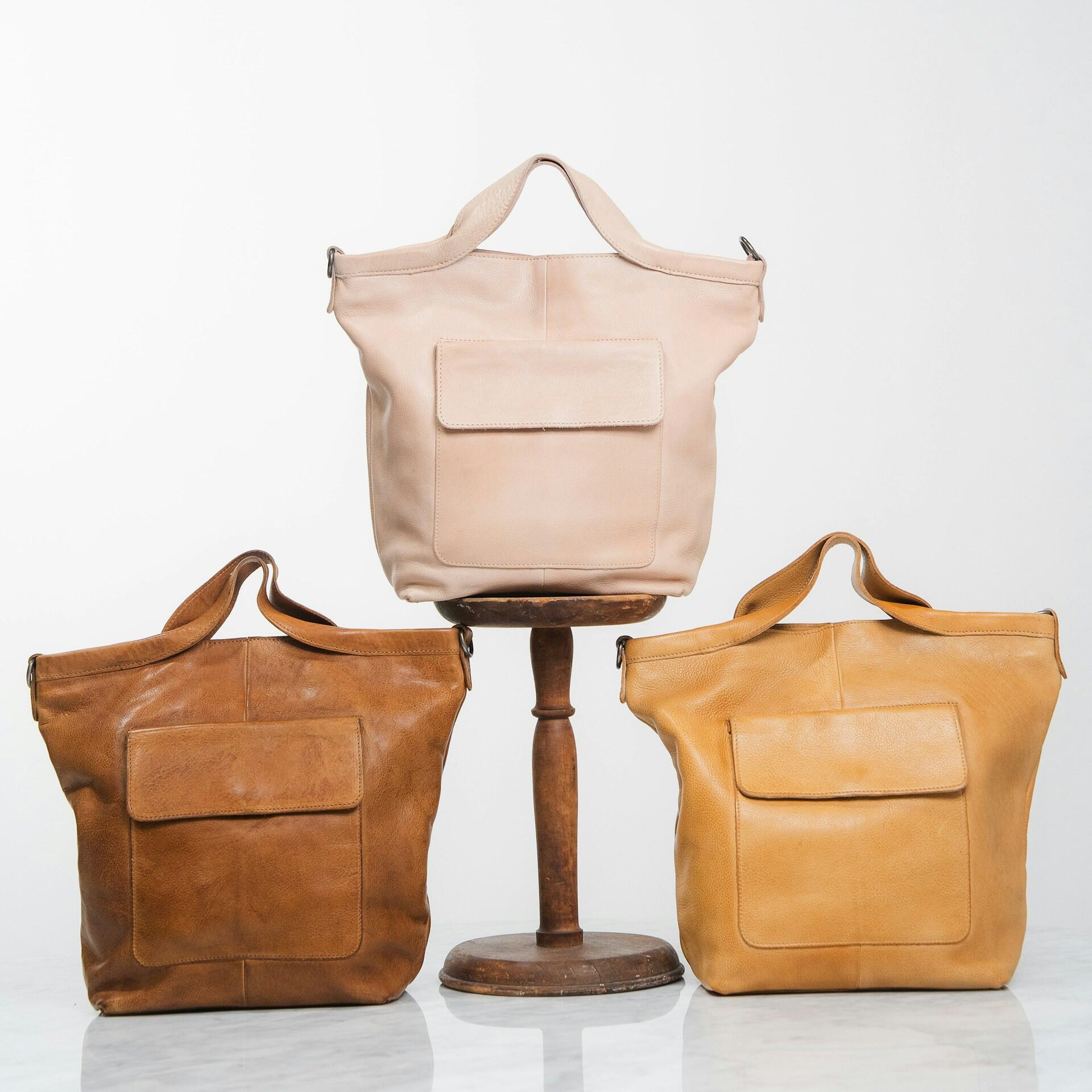 Three leather bags of similar style but different colours arranged in a white space. 