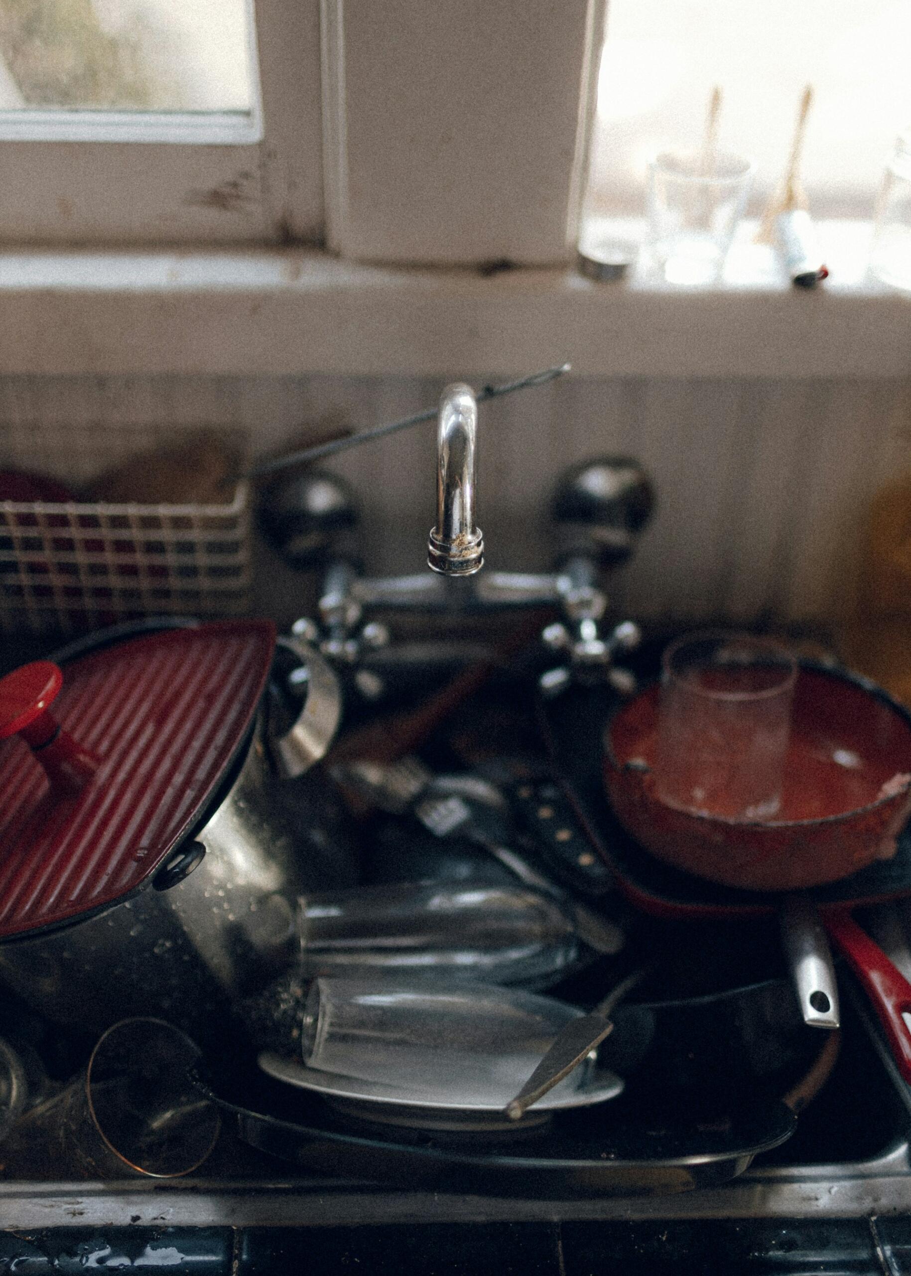 A kitchen sink full of dirty dishes, topped with a two-spigot, wall-mounted water tap.