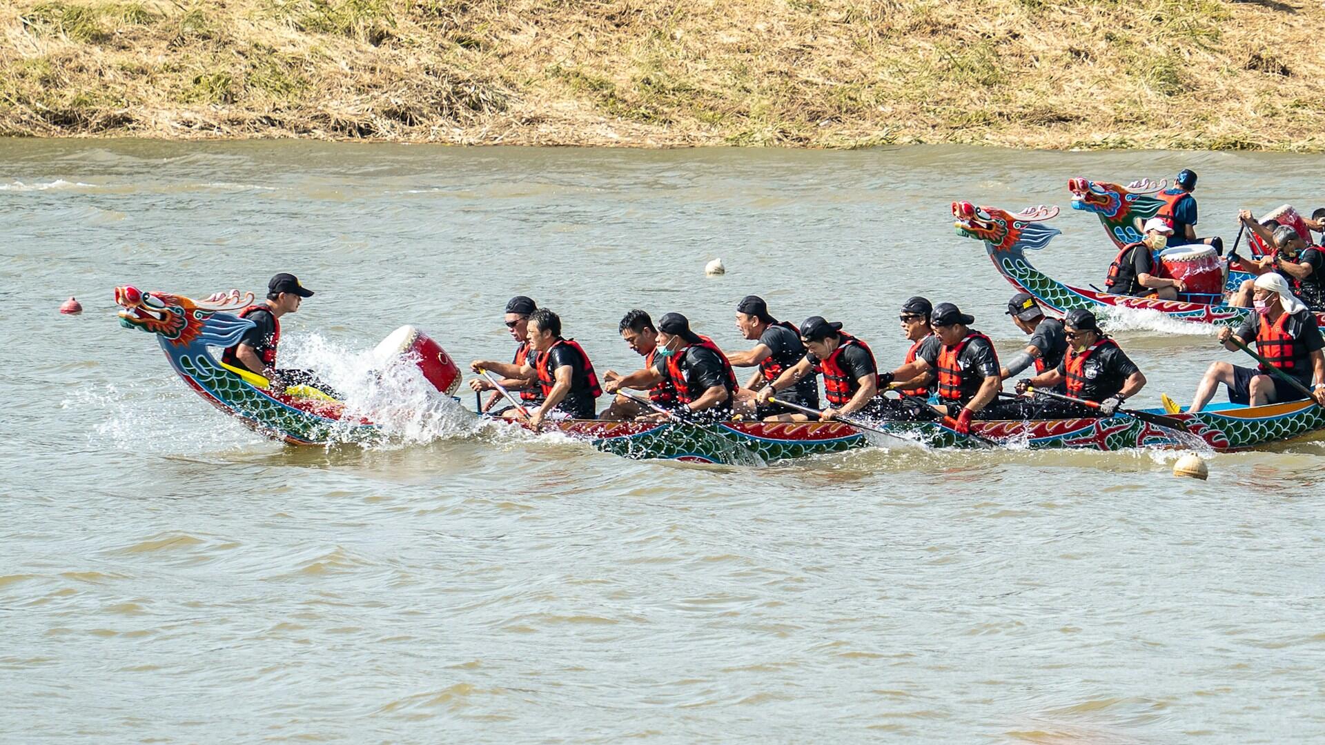 Dragon boat race with paddlers in black and red life vests paddling vigorously.