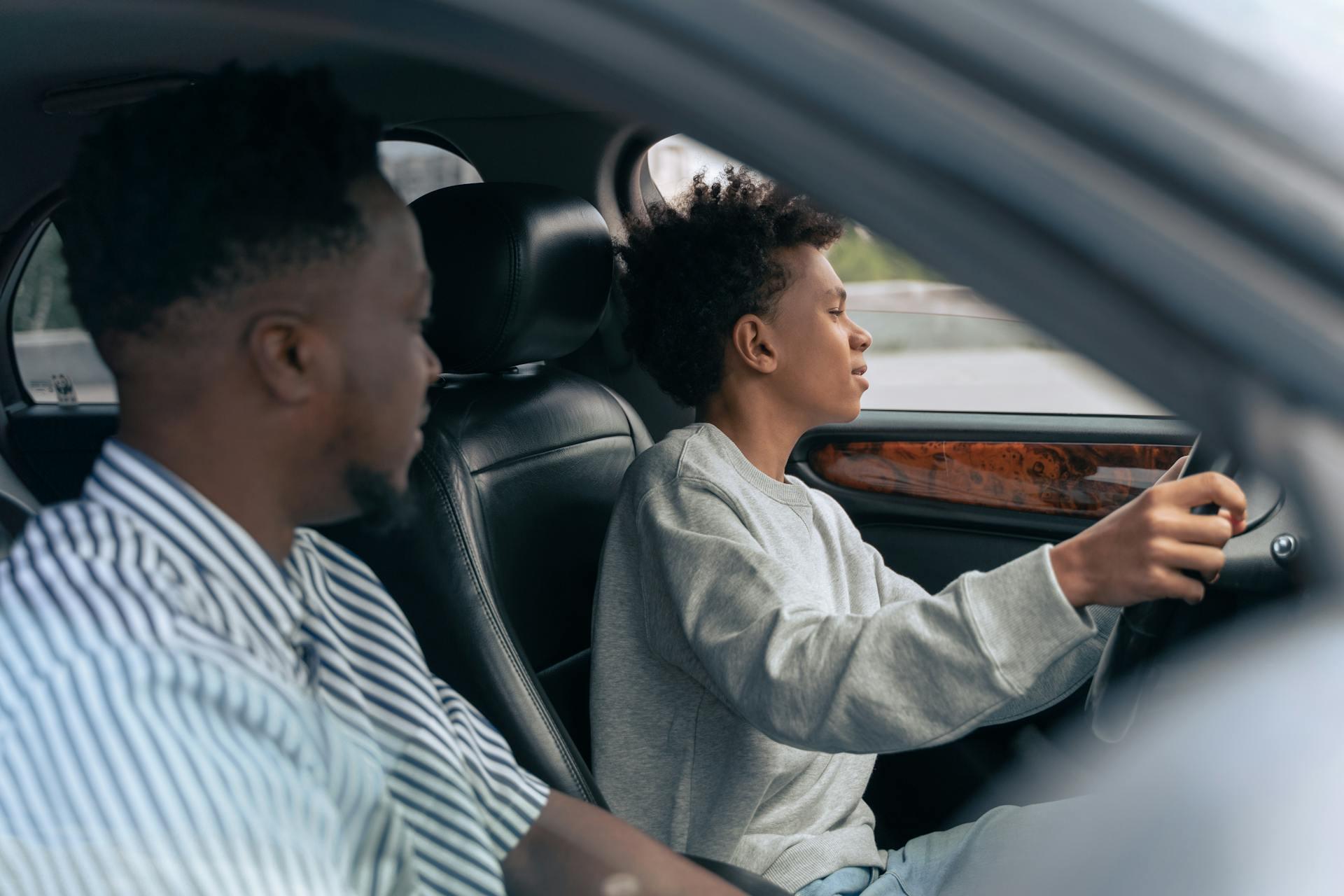 Two people inside a car, one seated behind the wheel driving, the other in the passenger seat looking ahead.