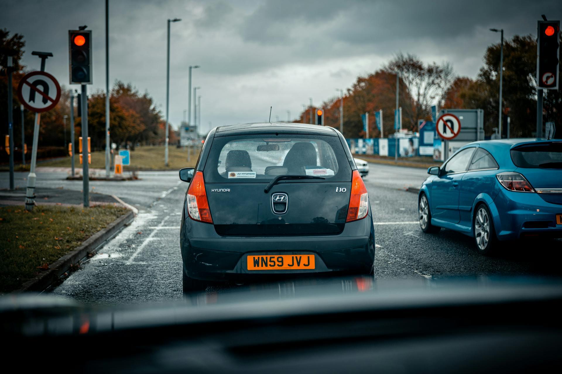 Cars stopped at a red light on a rainy road with no U-turn signs visible and autumn trees in the background.