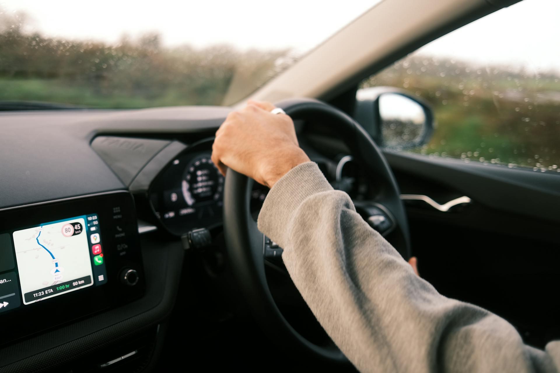 Person driving a car with GPS navigation showing route and speed limits on the dashboard screen on a rainy day.