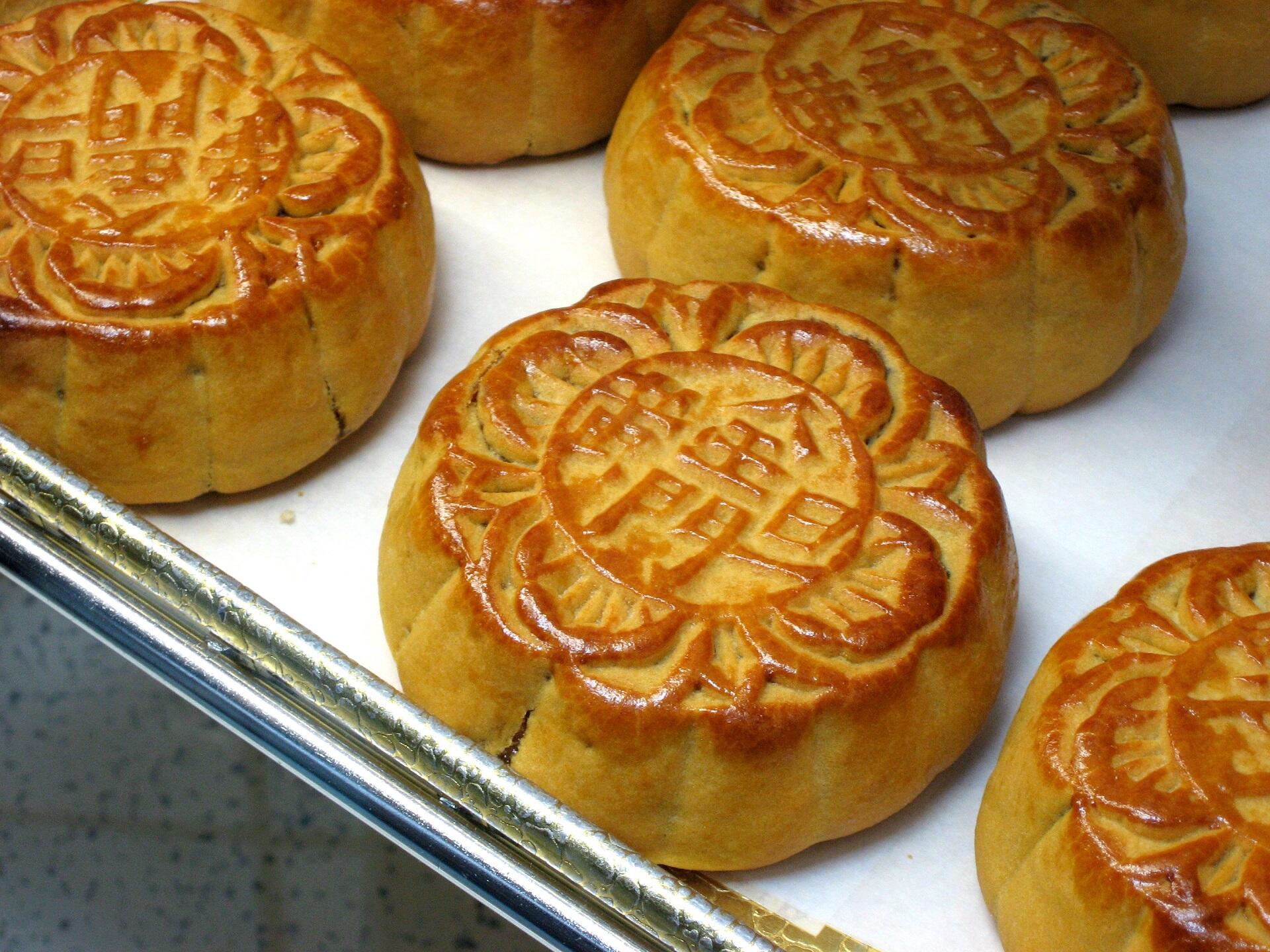 Golden brown mooncakes with intricate floral designs and Chinese characters are arranged on a baking tray.