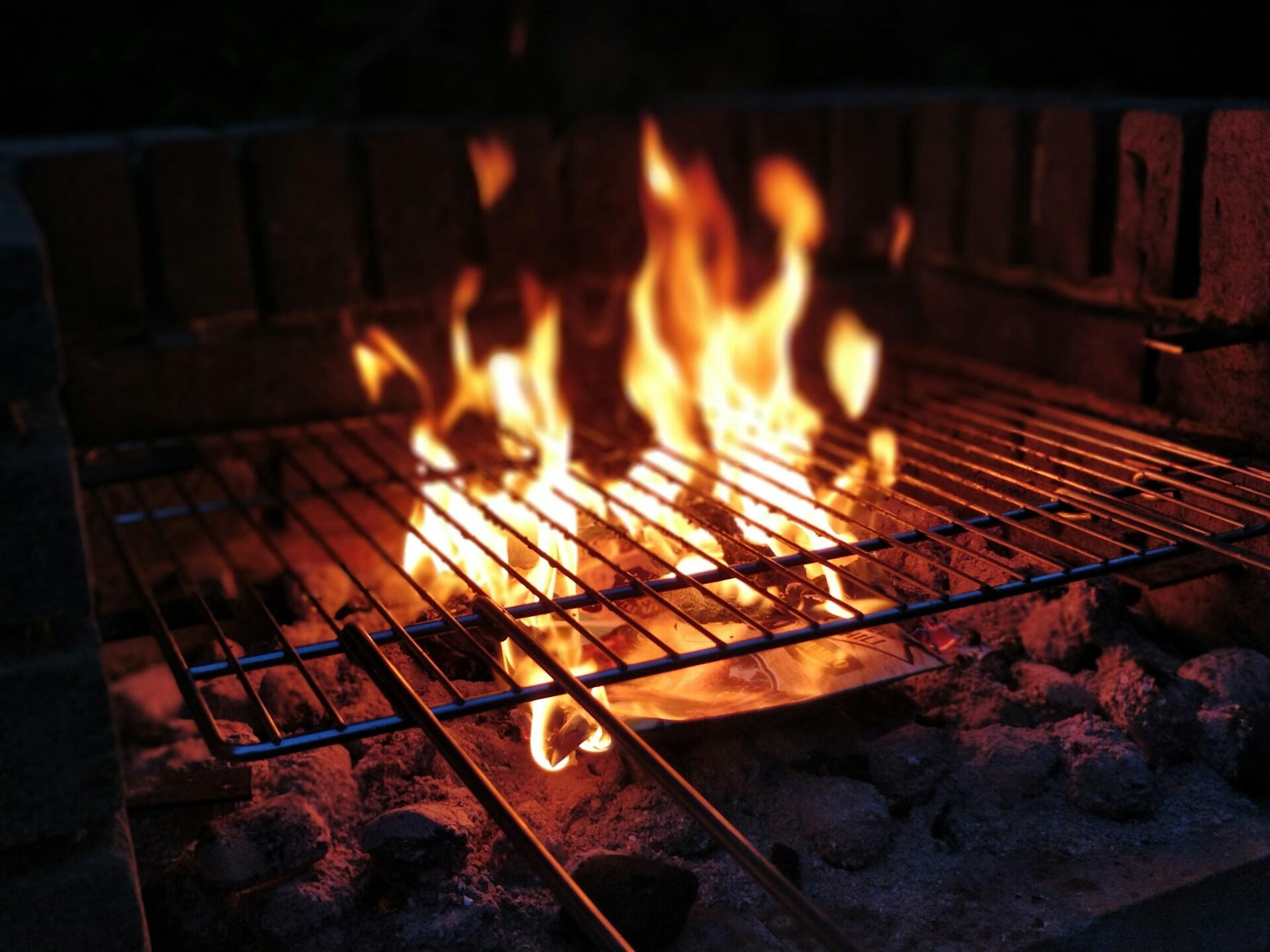 A charcoal grill with a rack in place and flames leaping past the rack.