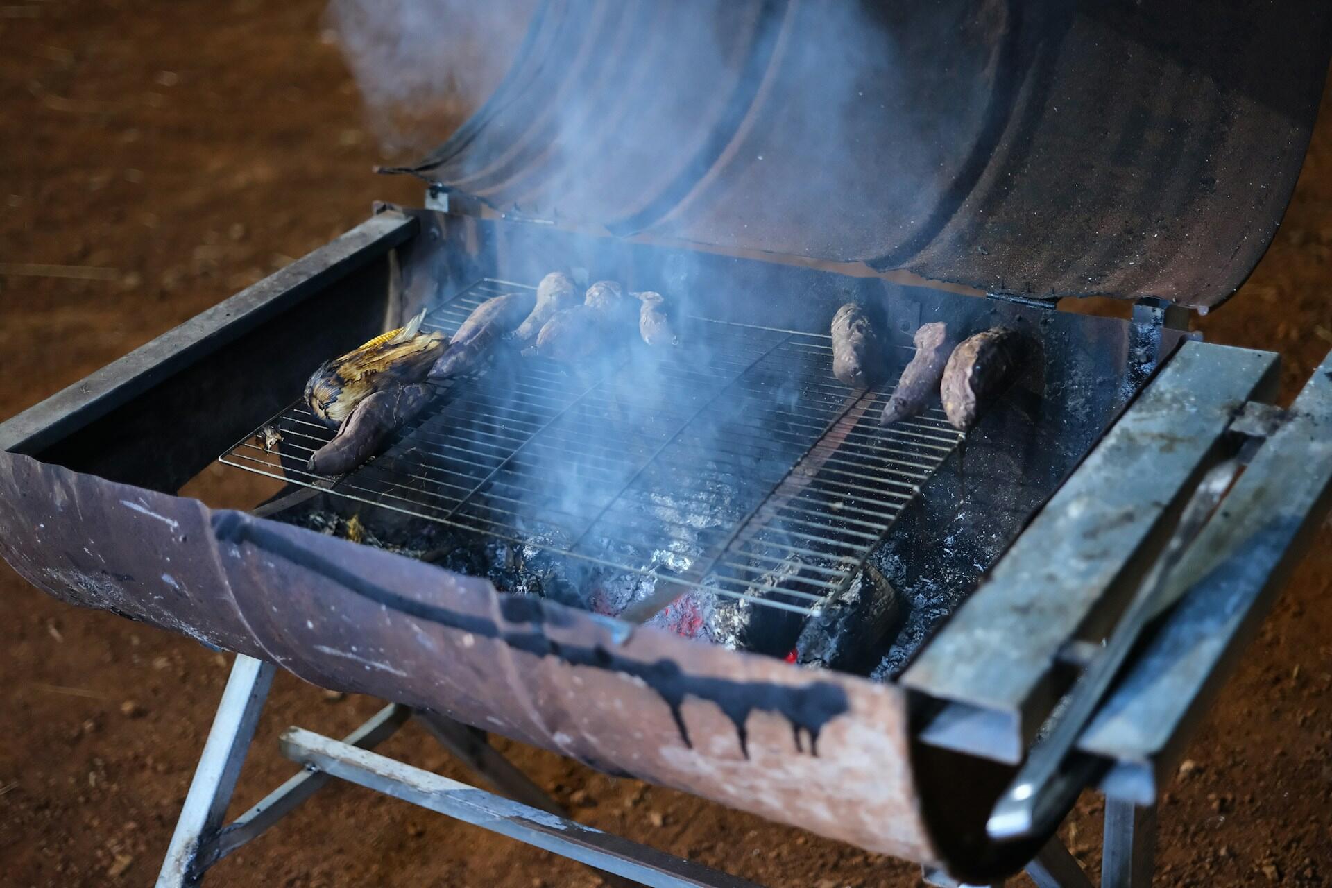 A metal oil drum cut in half longways to make a grill, with smoke coming out of it.