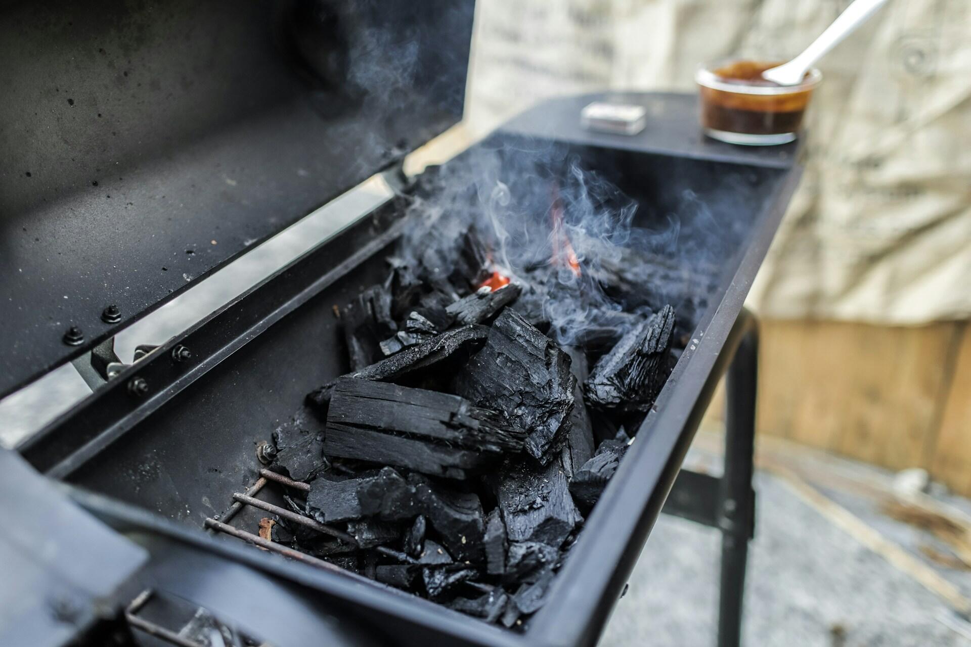 A black, opened grill with lump charcoal burning.
