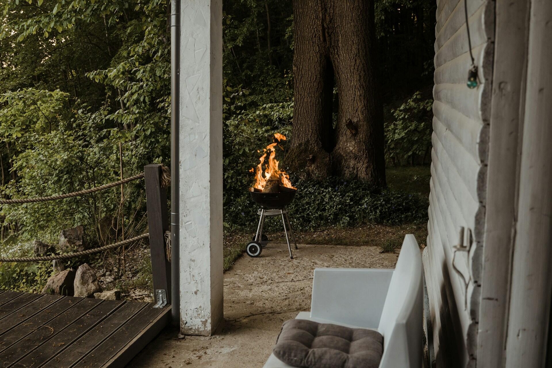 A black grill at the far end of a patio with a fairly large fire burning in it.