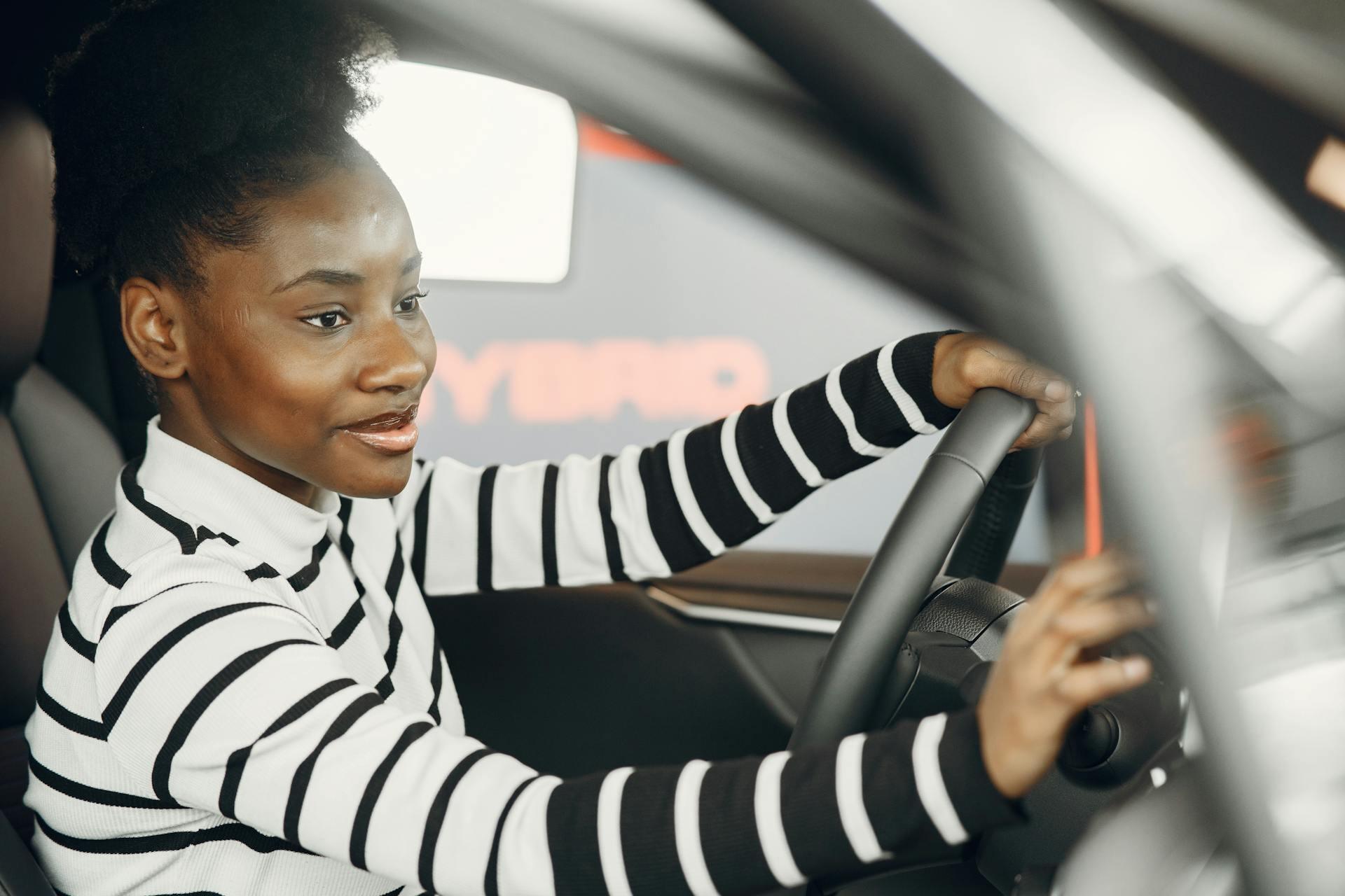 Person wearing a black and white striped sweater sits in the driver's seat, holding the steering wheel of a car.