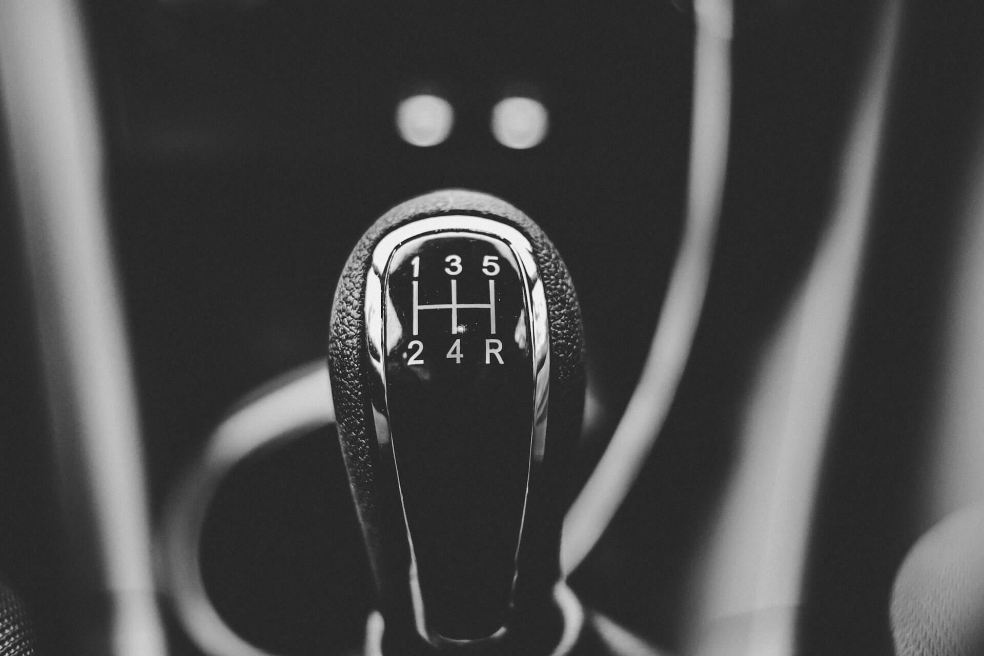 Close-up black and white image of a manual car gear shift knob showing 5-speed pattern with reverse gear.