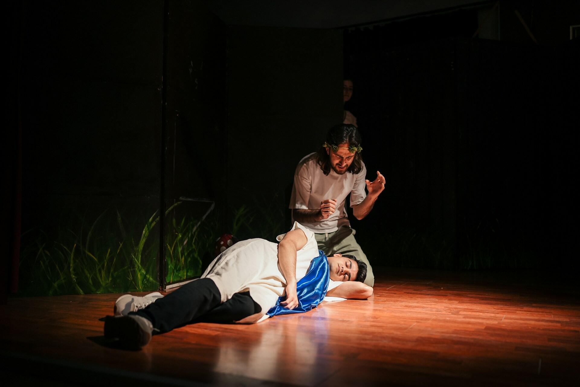 actors portraying a scene from a Shakespeare work, with one giving a monologue over the other who s laying on the floor