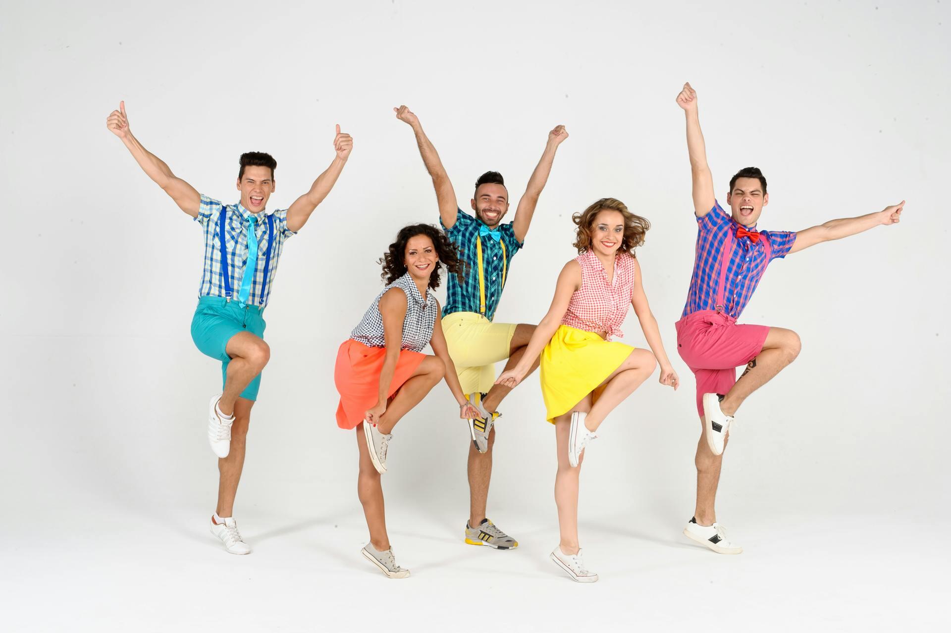 group of adult theatre performers dressed in bright clothes and dancing