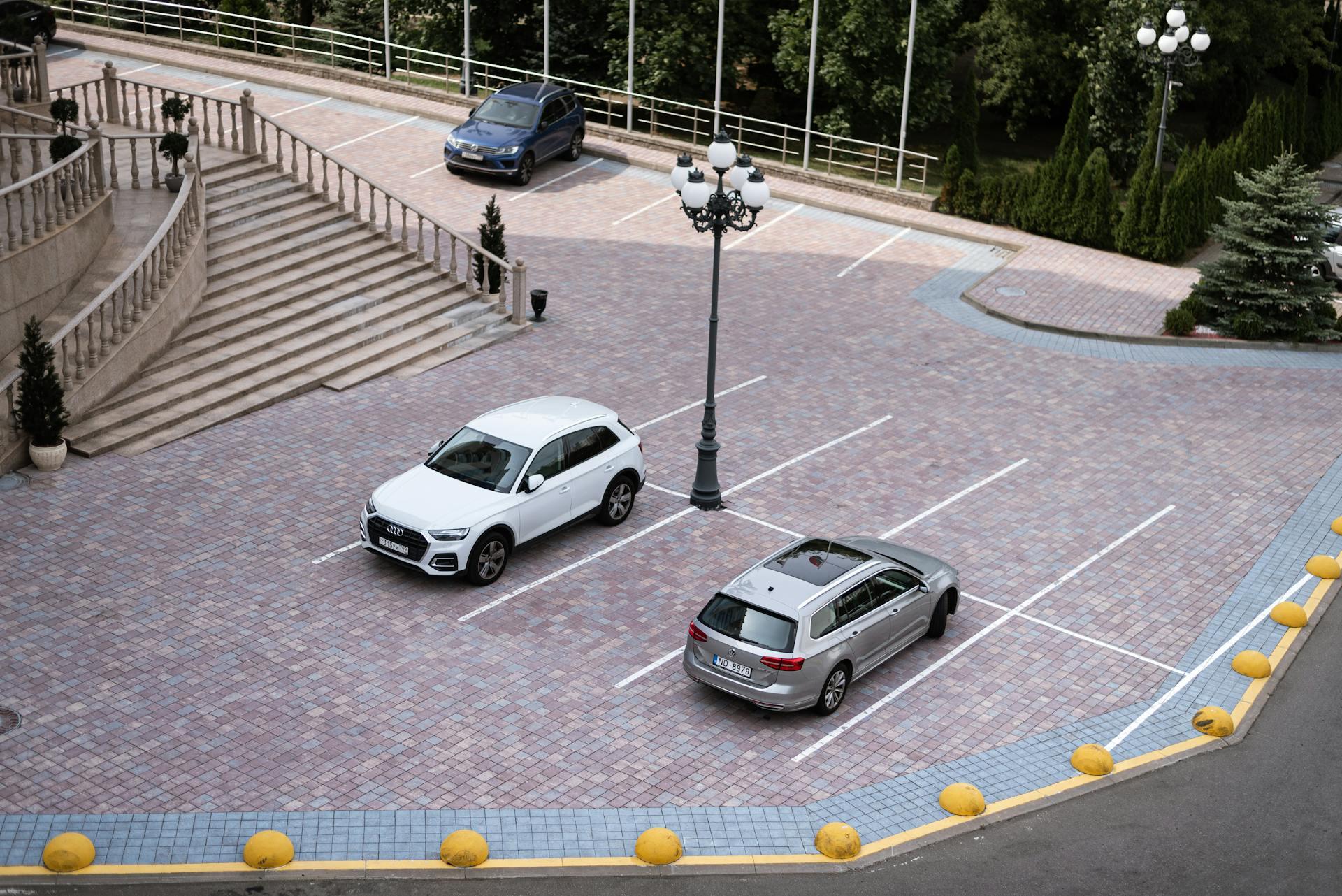 A nearly empty parking lot with three parked cars on a paved surface near a staircase and trees.