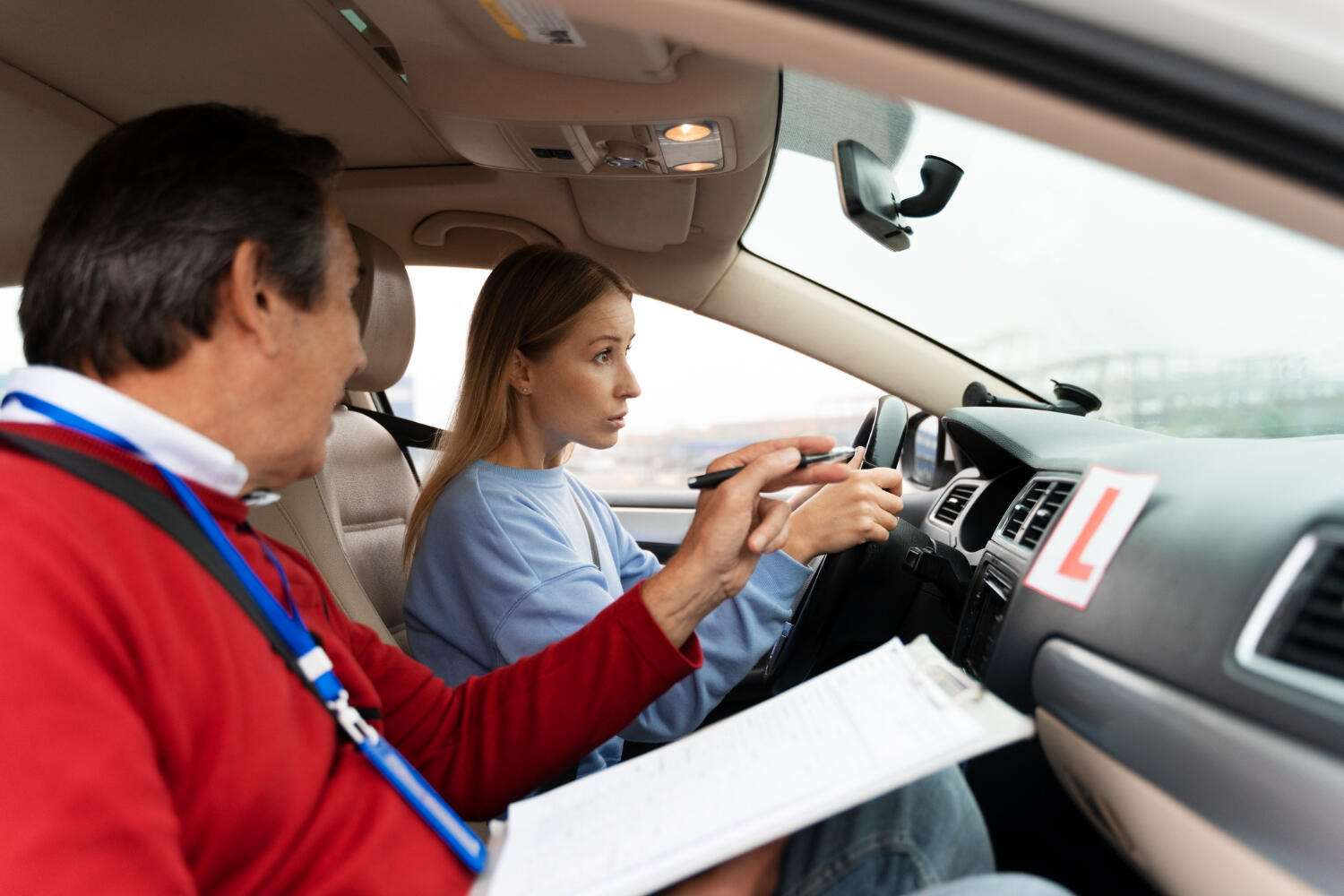 Driving instructor giving directions to student driver in a car with learner driver