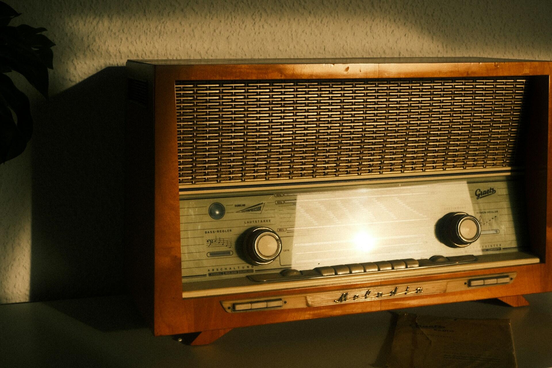 Vintage wooden tube radio with a woven speaker grille and illuminated tuning dial illuminated by warm, dramatic light.