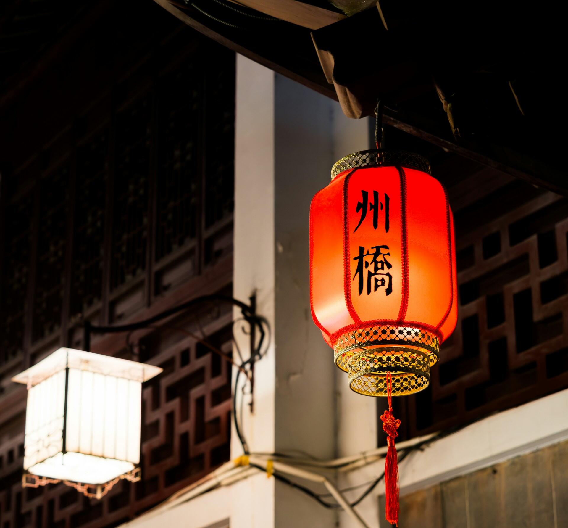 A red Chinese lantern with black writing on it hanging in the night.