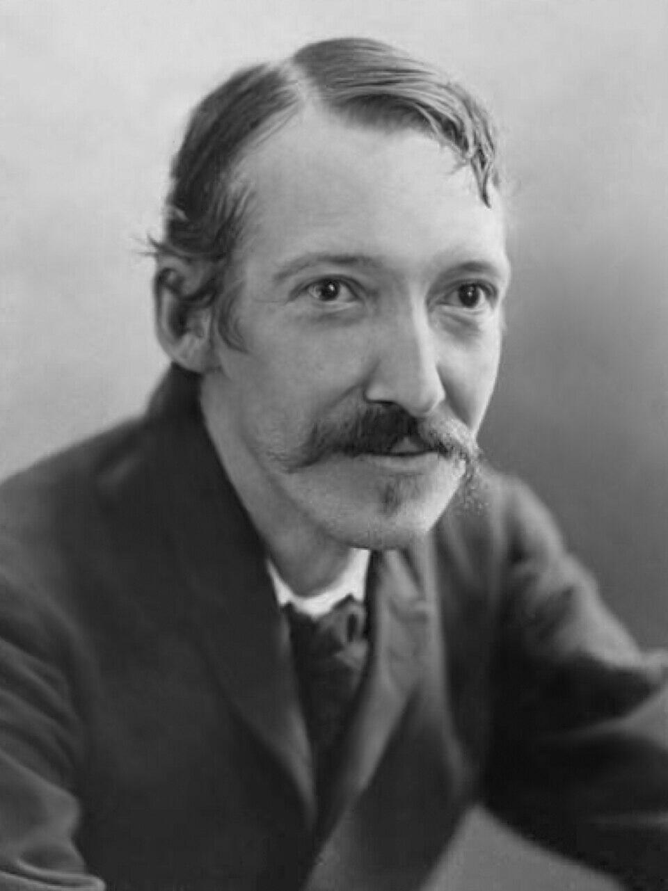 Black and white portrait of a man with slicked-back hair and a prominent, curled mustache wearing a dark suit.