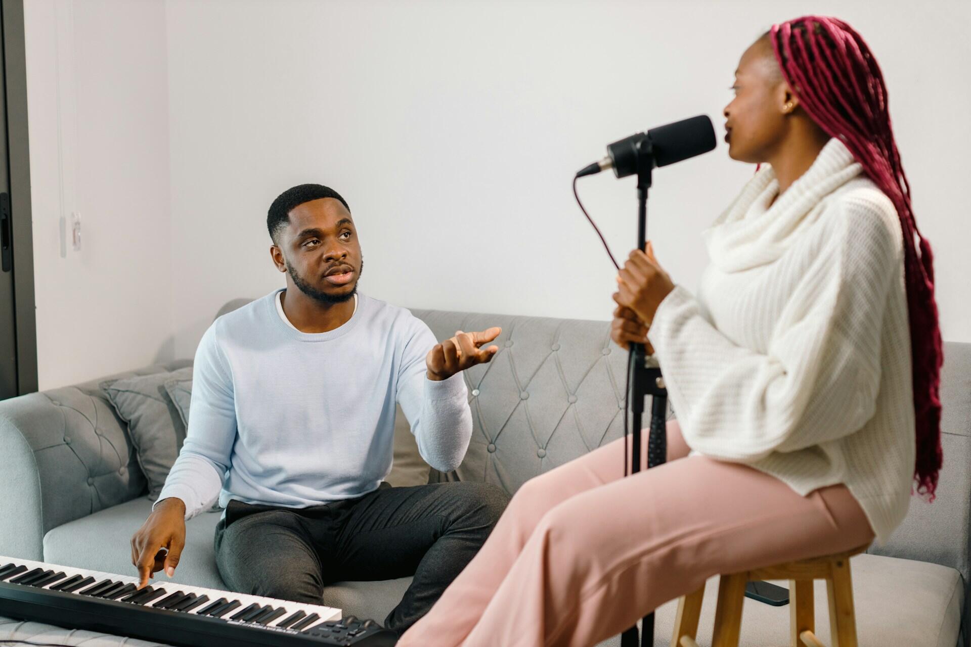 a voice student listening to advice from her vocal coach, who plays the piano to accompany the student
