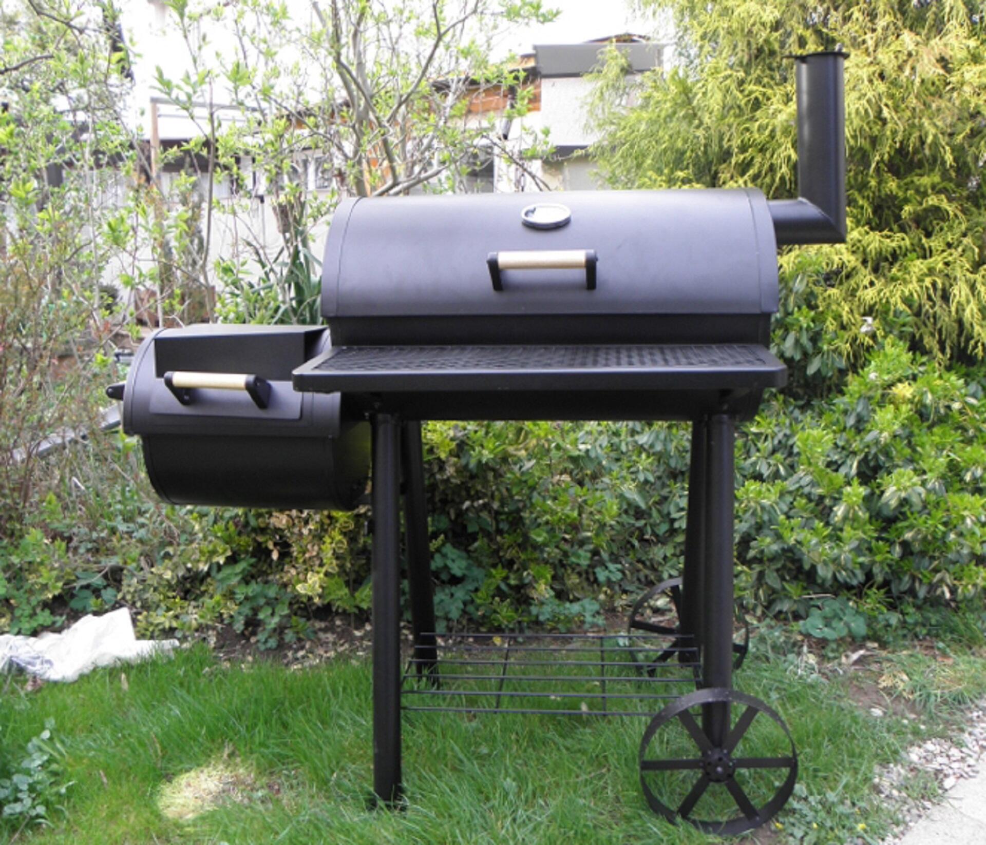 A black grill in a green garden with a black smoker box attached.