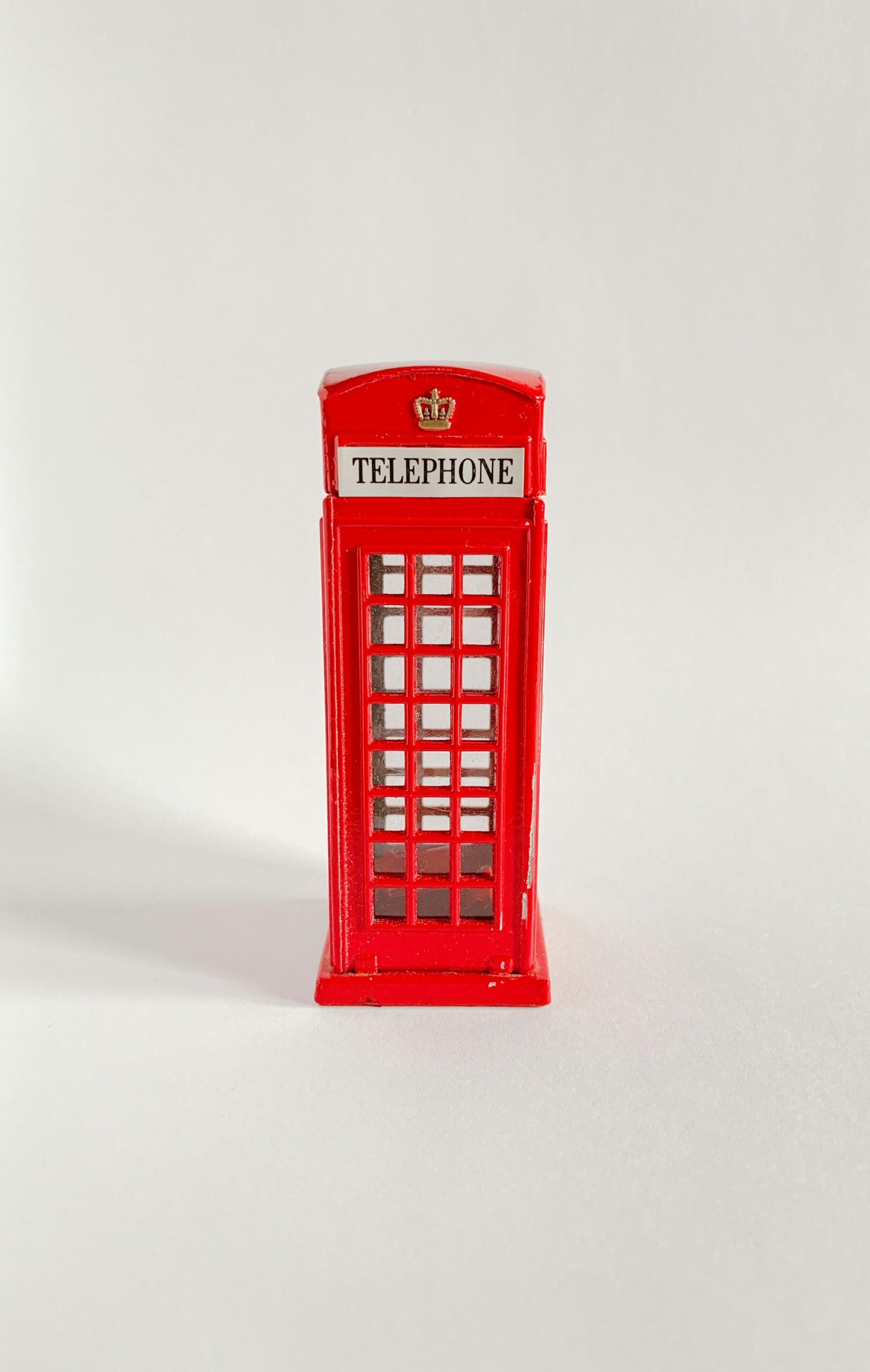 Miniature red British telephone booth sits centered against a plain white background.
