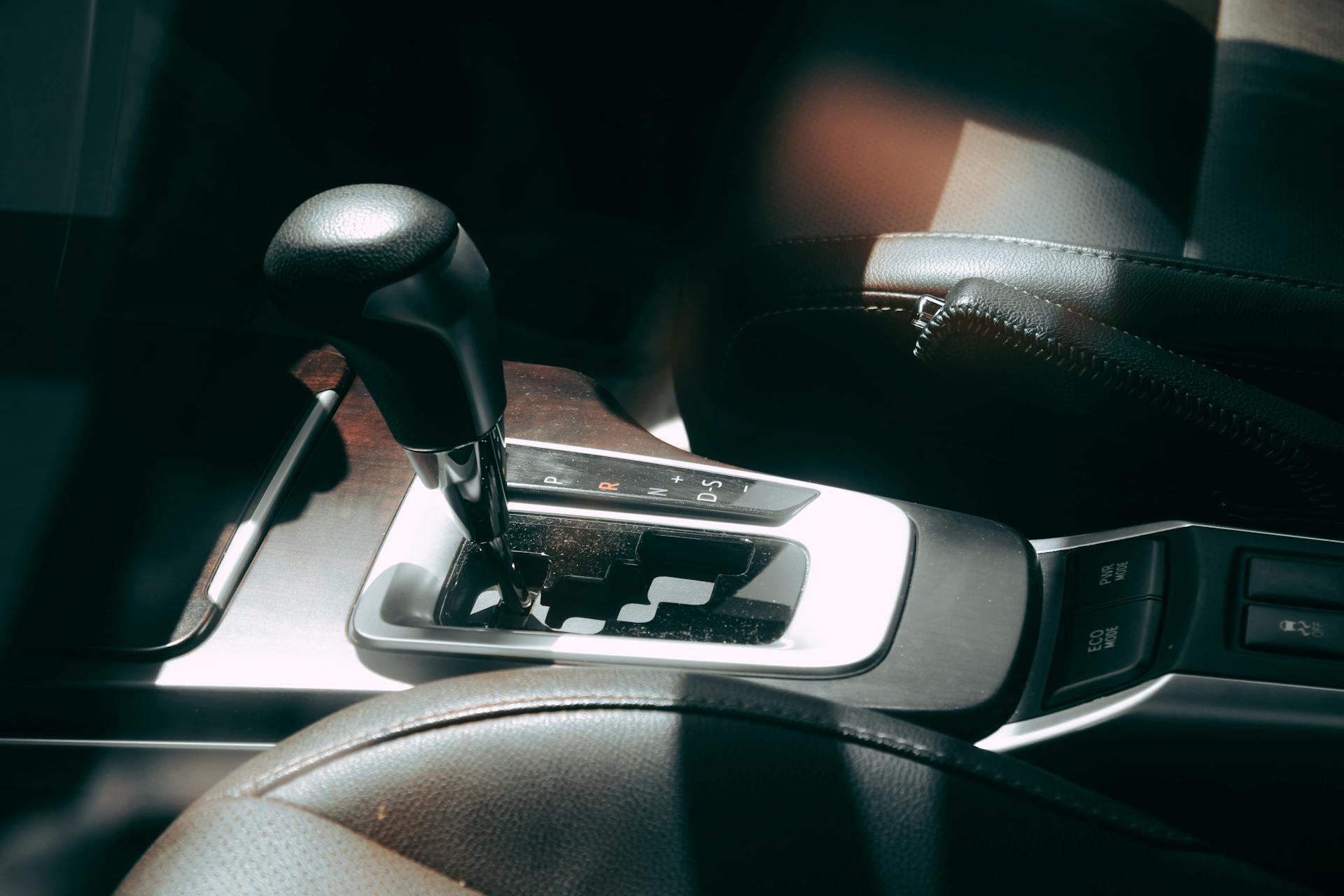 Close-up of a car's automatic gear shift lever and surrounding console with leather seats and mode buttons.