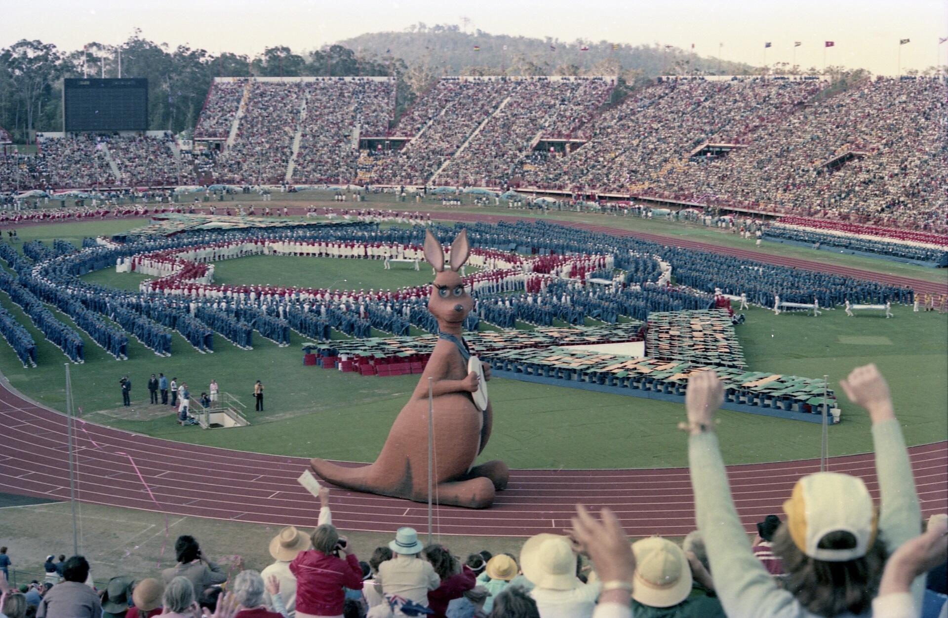 An open-air stadium with full stands and people on the field wearing formal uniforms, arranged in a distinctive pattern. 