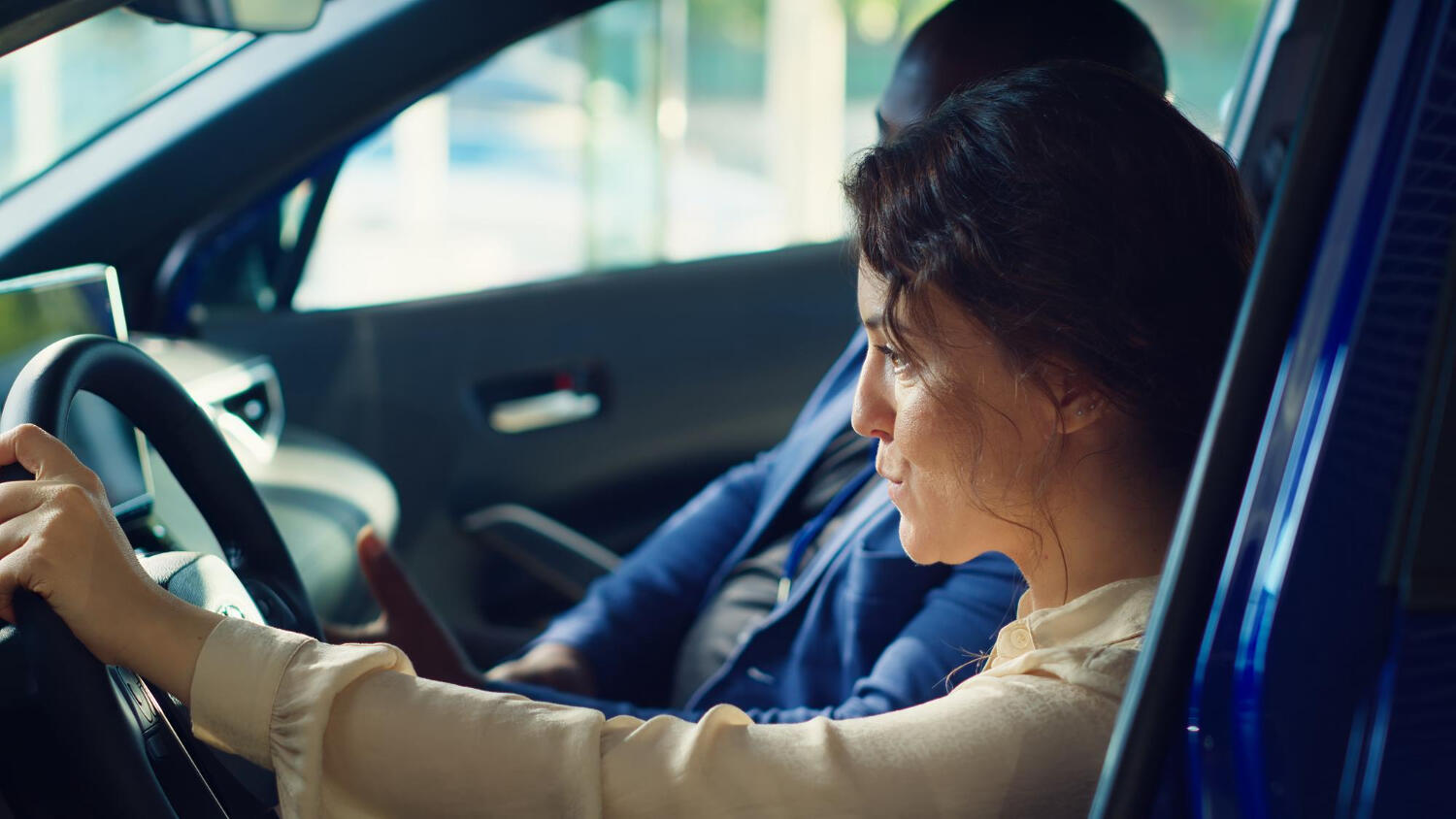 Two people inside a car, one holding the steering wheel and the other gesturing while seated beside the driver.