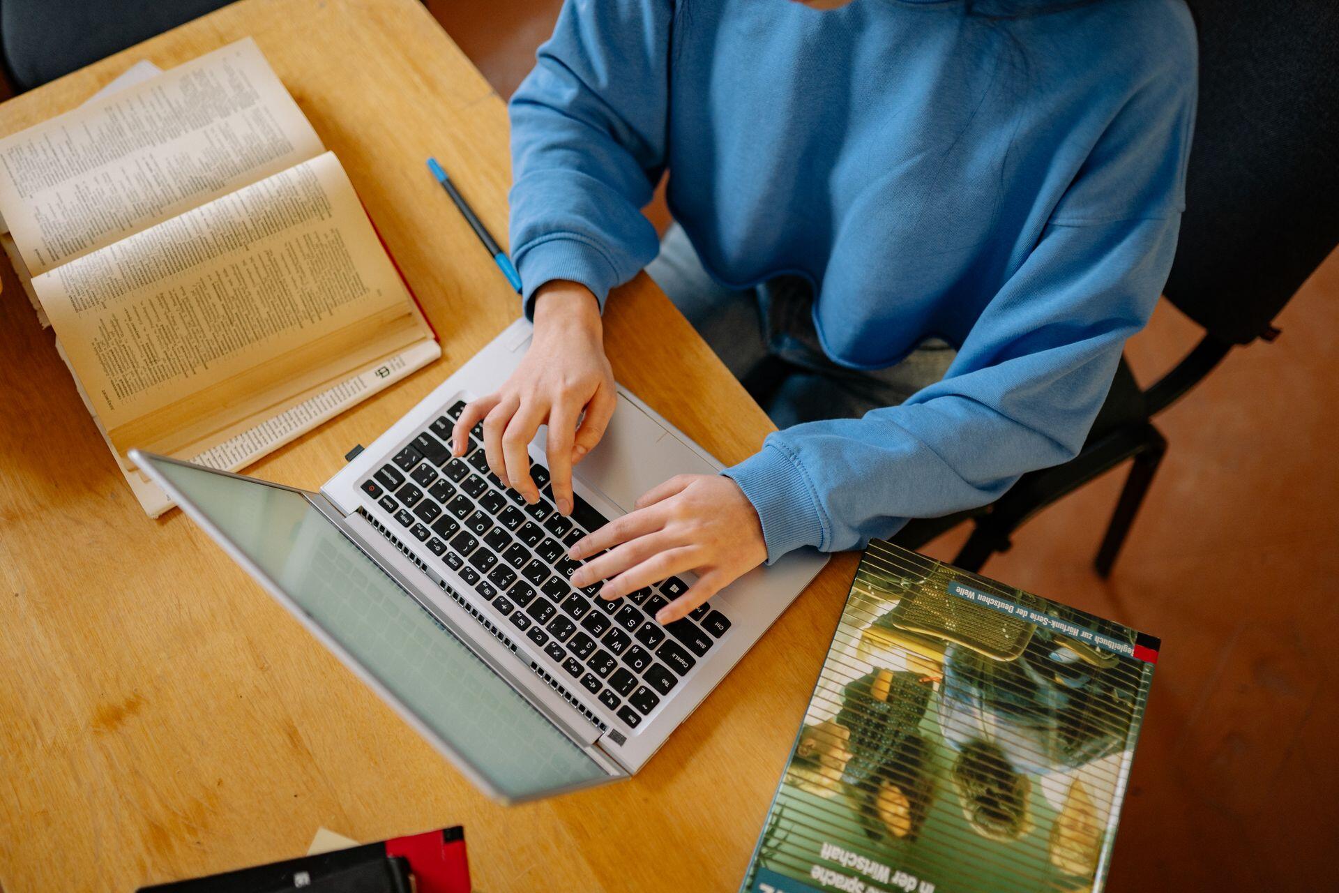 Man in blue sweater sitting at a desk typing on computer
