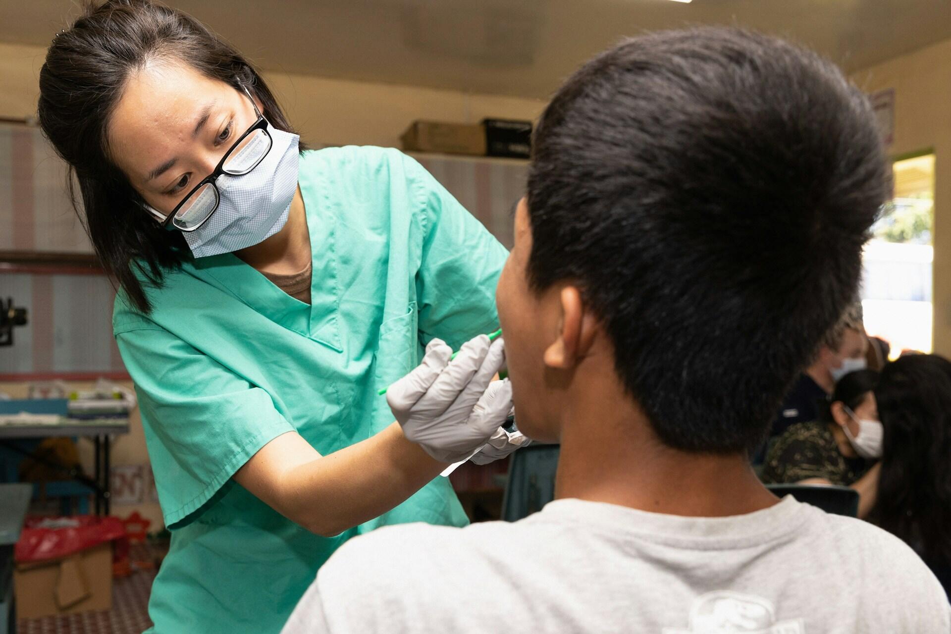 Dental worker in green scrubs and a face mask examining a patient’s mouth