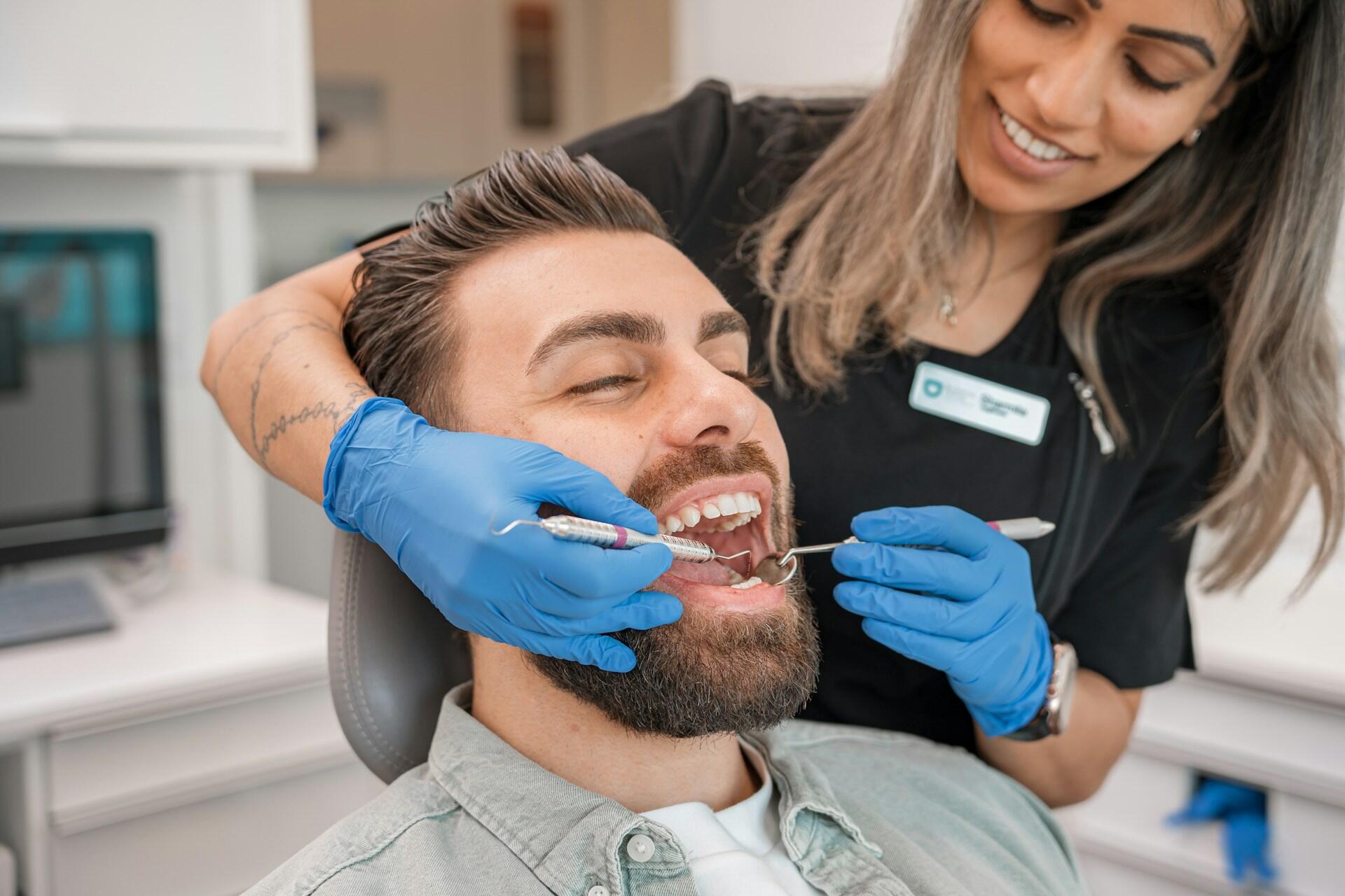 A dental professional examining a smiling patient in a dental chair