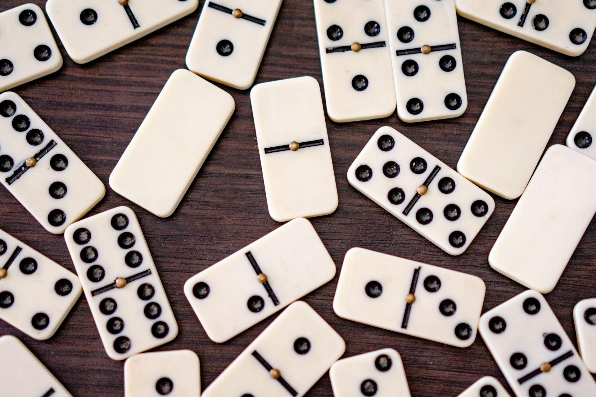 Scattered white domino tiles with black dots and wooden connectors on a dark wooden surface.