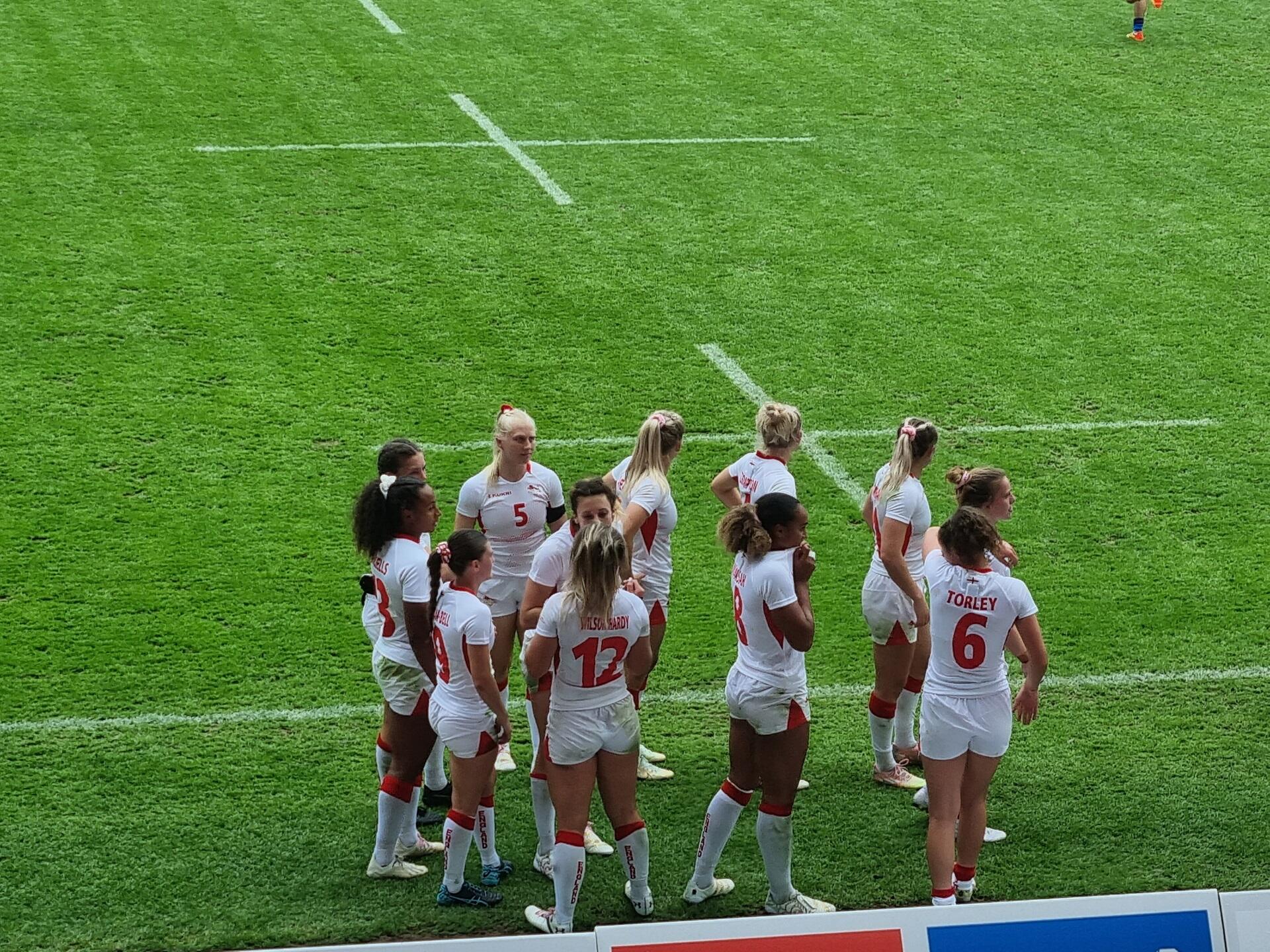 Women on a rugby pitch wearing red and white uniforms.