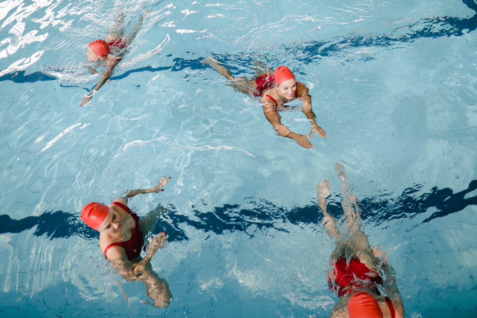 4 swimmers in red swim wear swimming in a pool