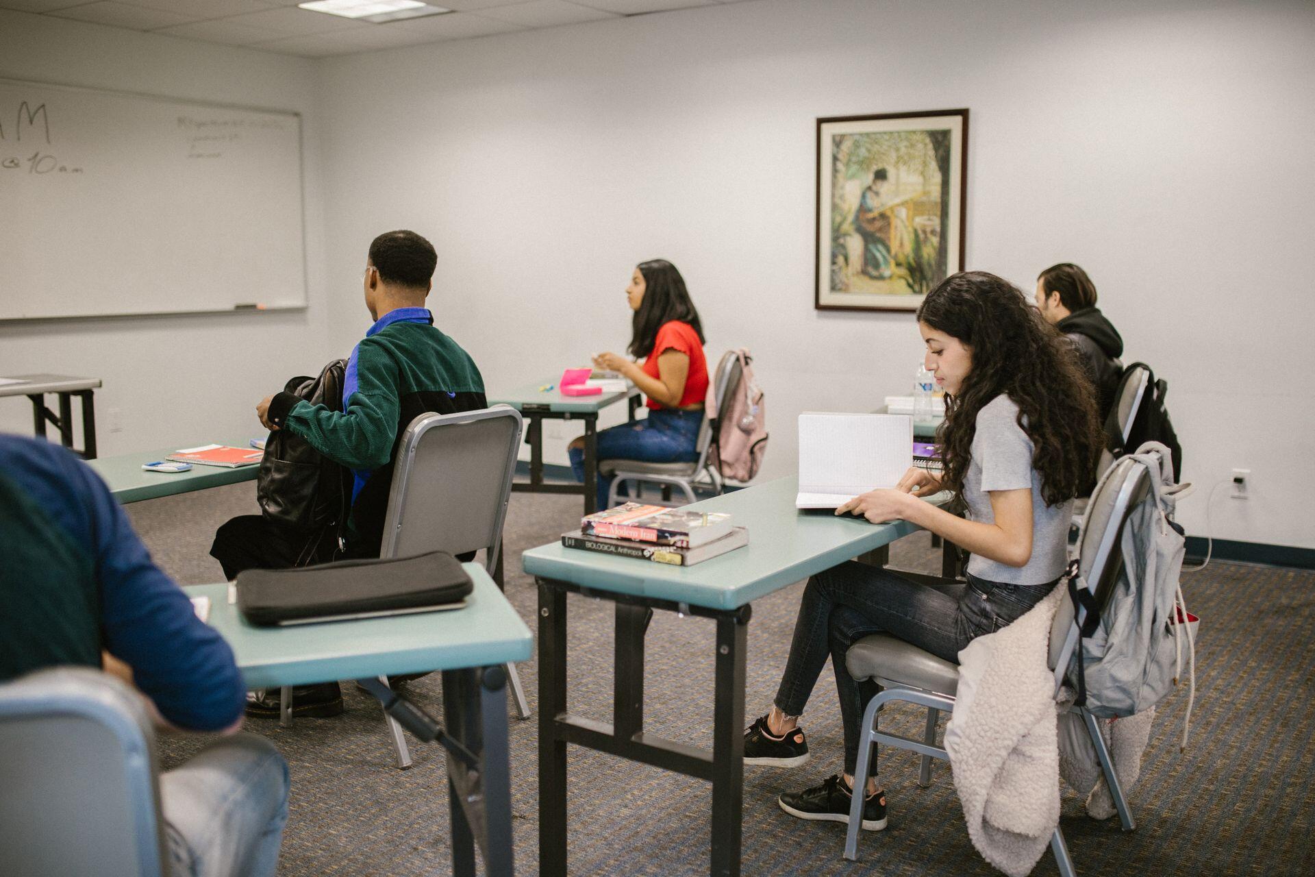 Students seated at individual desks in a classroom, engaged in reading and organizing their materials during a study session.