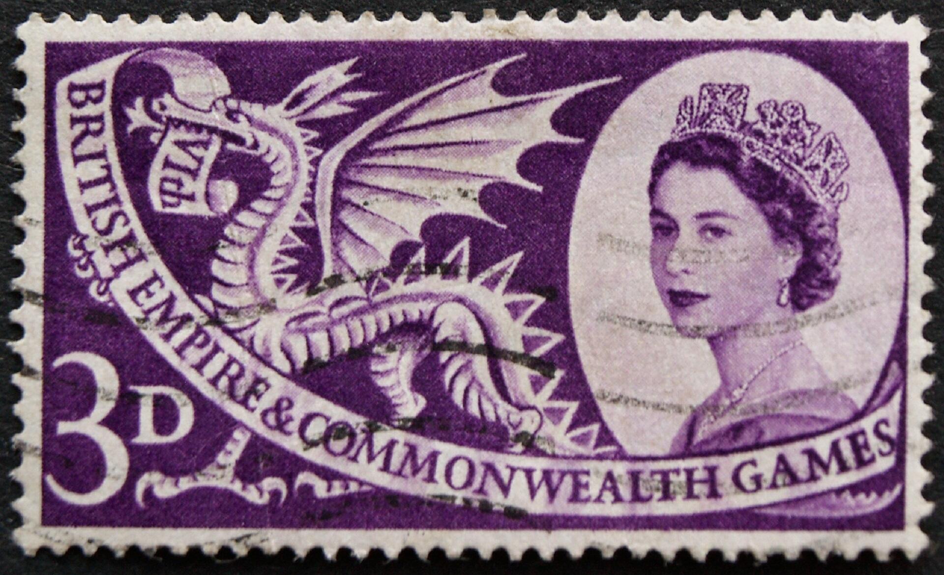 A purple and white postage stamp featuring young Queen Elizabeth II, a dragon, and a banner touting the Commonwealth Games.